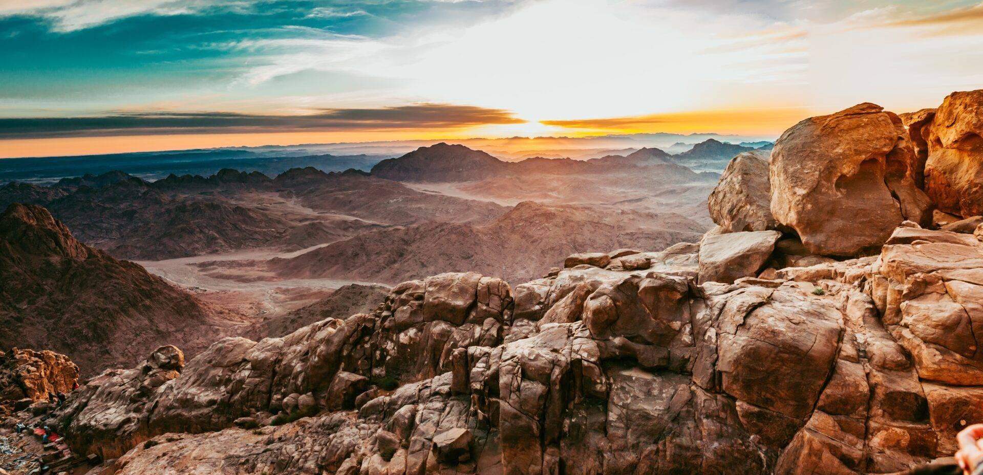 Vista panoramica di un deserto montagnoso roccioso al tramonto, con formazioni di granito in primo piano