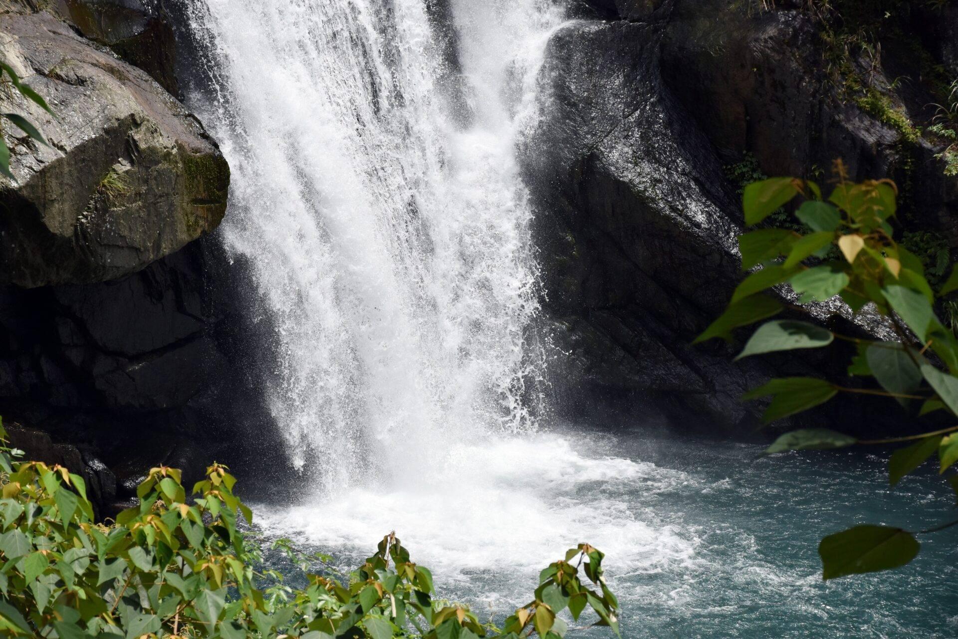 Una cascata potente si riversa in una vasca turchese circondata da rocce muschiose e vegetazione lussureggiante