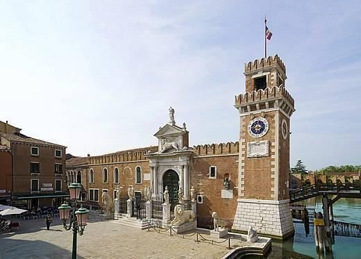 Una piazza storica veneziana con una torre dell’orologio in mattoni e un edificio classico in pietra vicino a un canale
