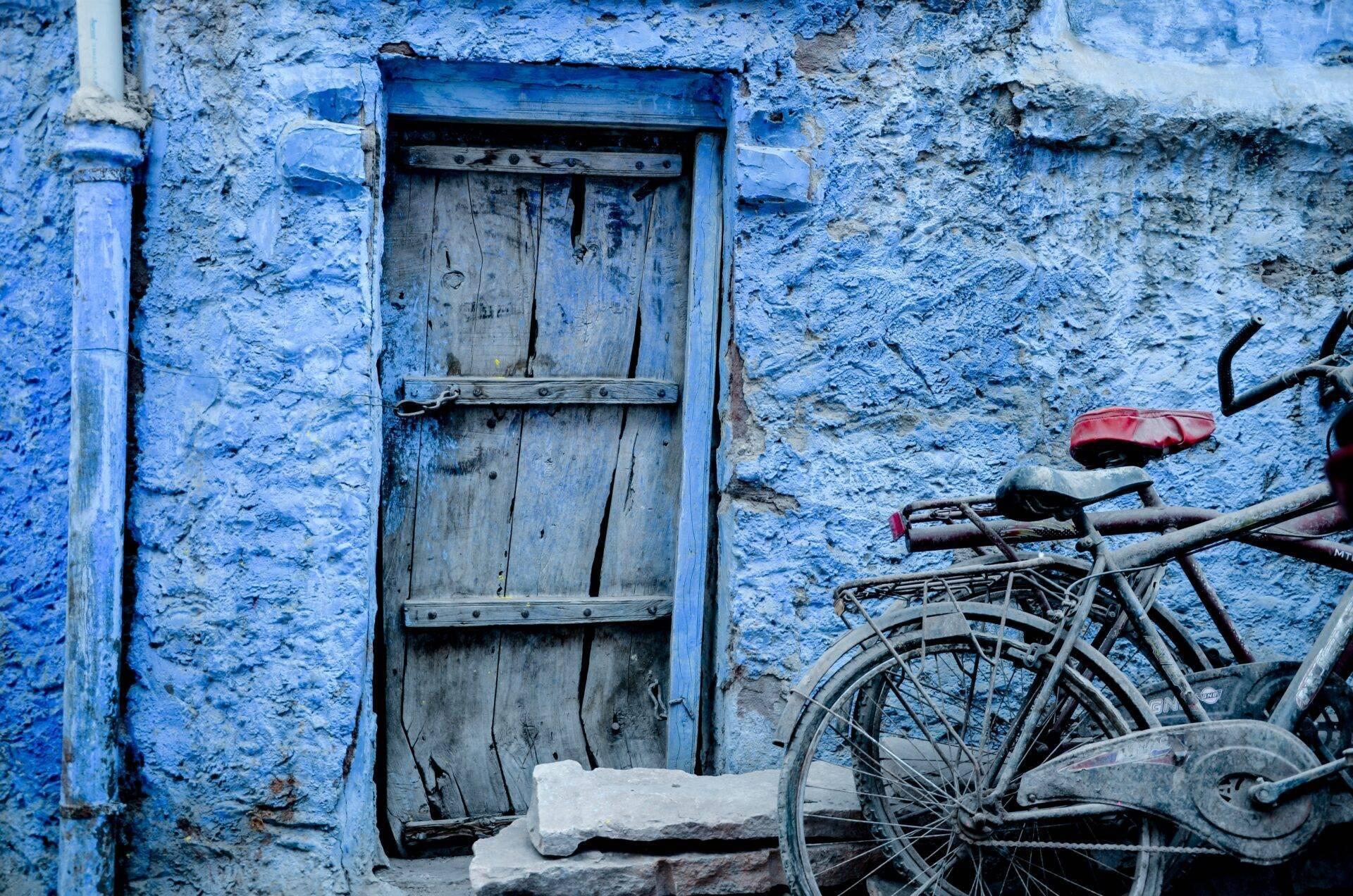 Porta in legno blu su un muro dipinto di una città vecchia con una bicicletta arrugginita appoggiata al muro