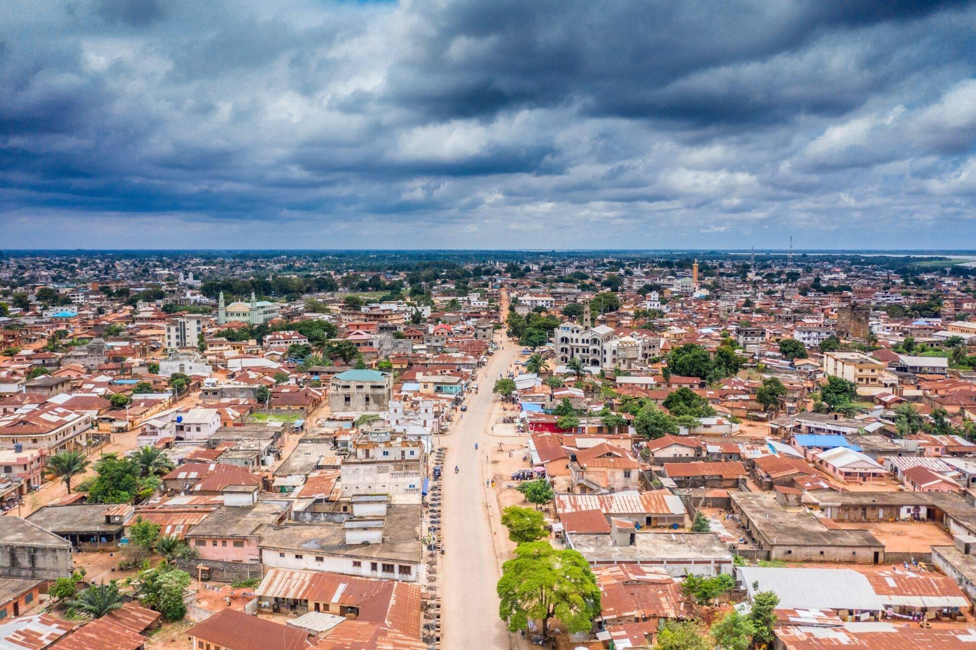 Aerial view of an African town with colourful buildings, red rooftops and a main street under a cloudy sky