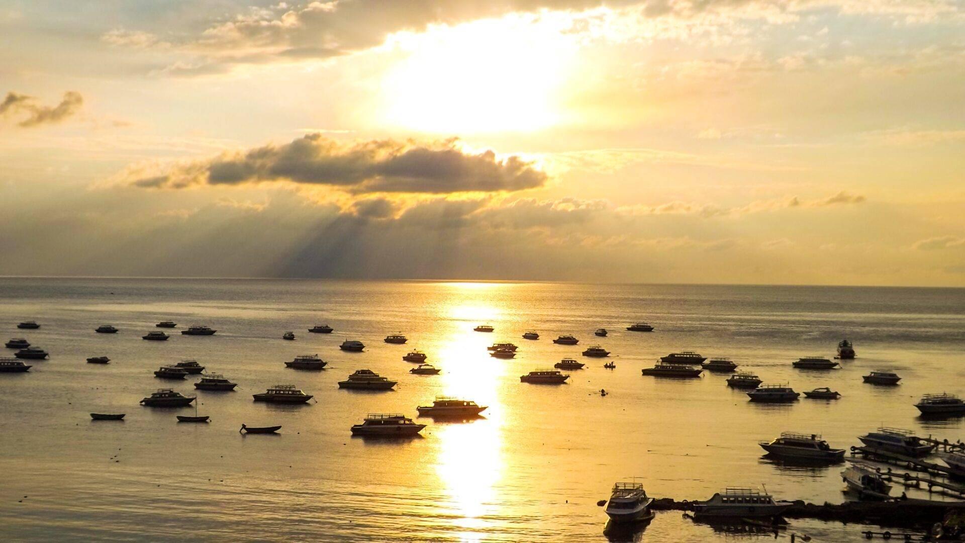 Tramonto dorato su una baia con numerose imbarcazioni da pesca ancorate in acque calme