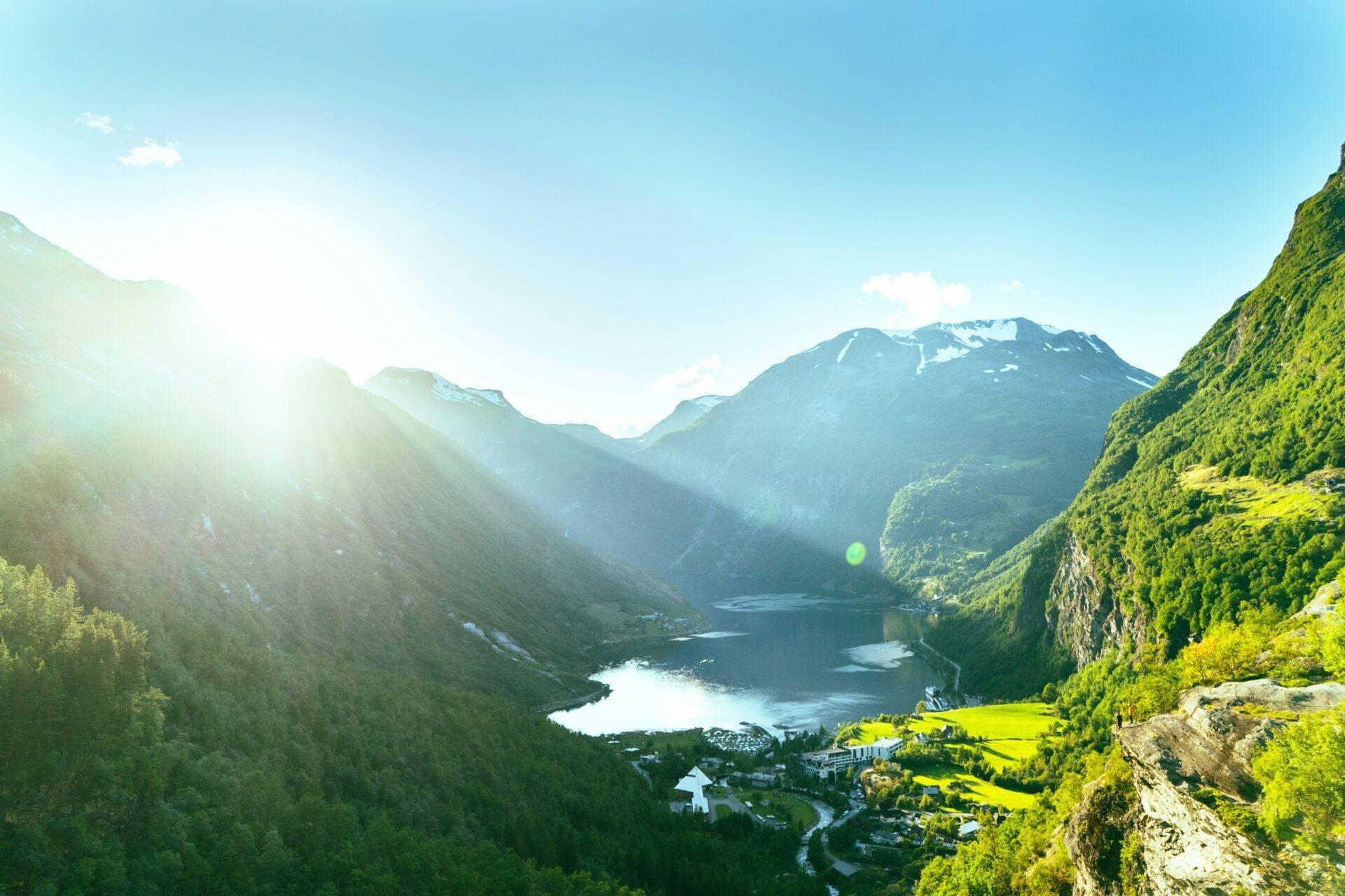 Alpine Tallandschaft mit eingebettetem blauen See zwischen bewaldeten Bergen und verschneiten Gipfeln bei Sonnenschein