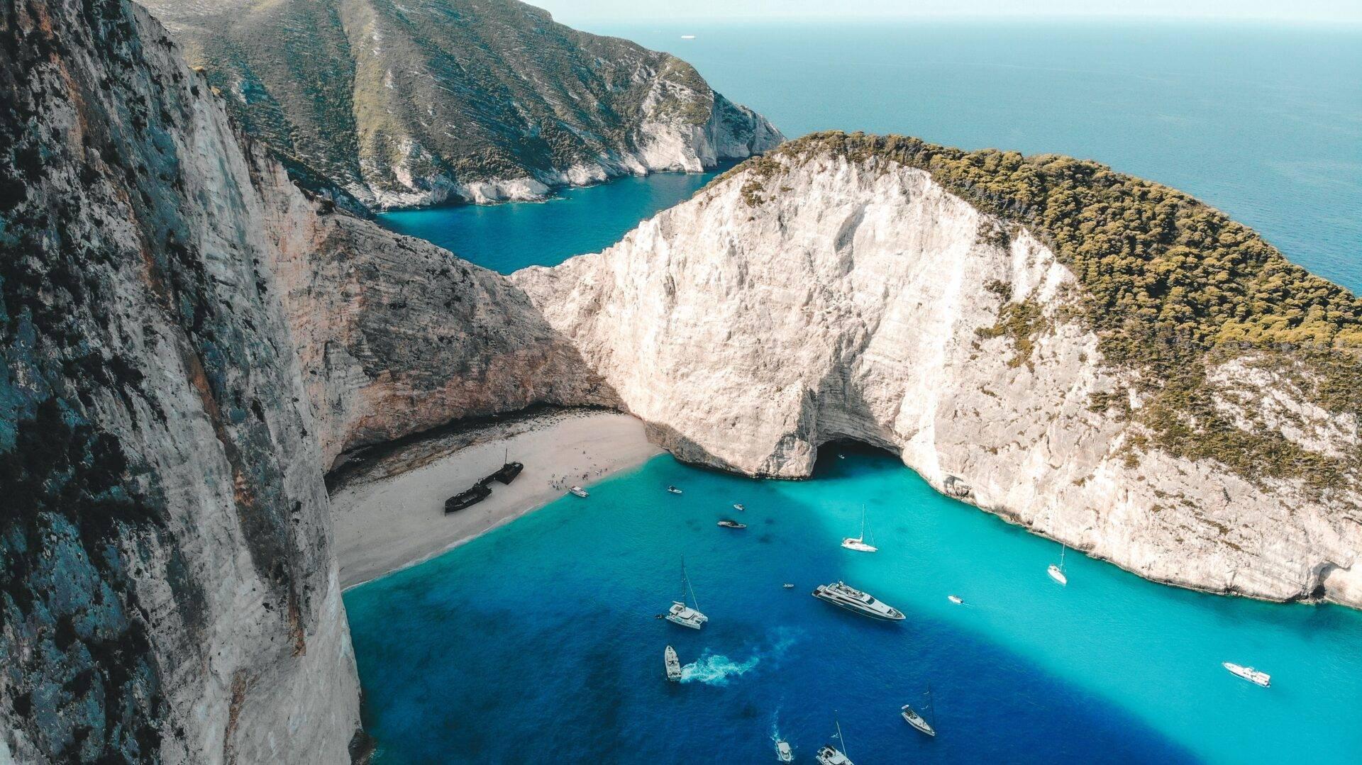 Luftaufnahme einer türkisfarbenen Bucht, eingerahmt von weißen Klippen, mit Strand und ankernden Booten