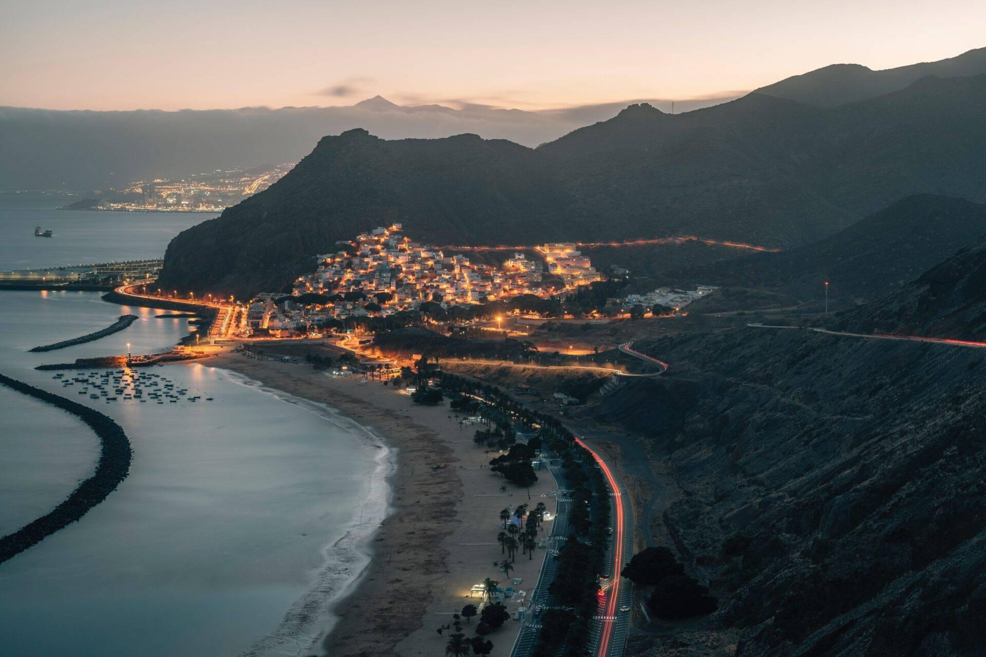 Vista aerea al crepuscolo di una piccola città costiera illuminata incorniciata da montagne e dal mare