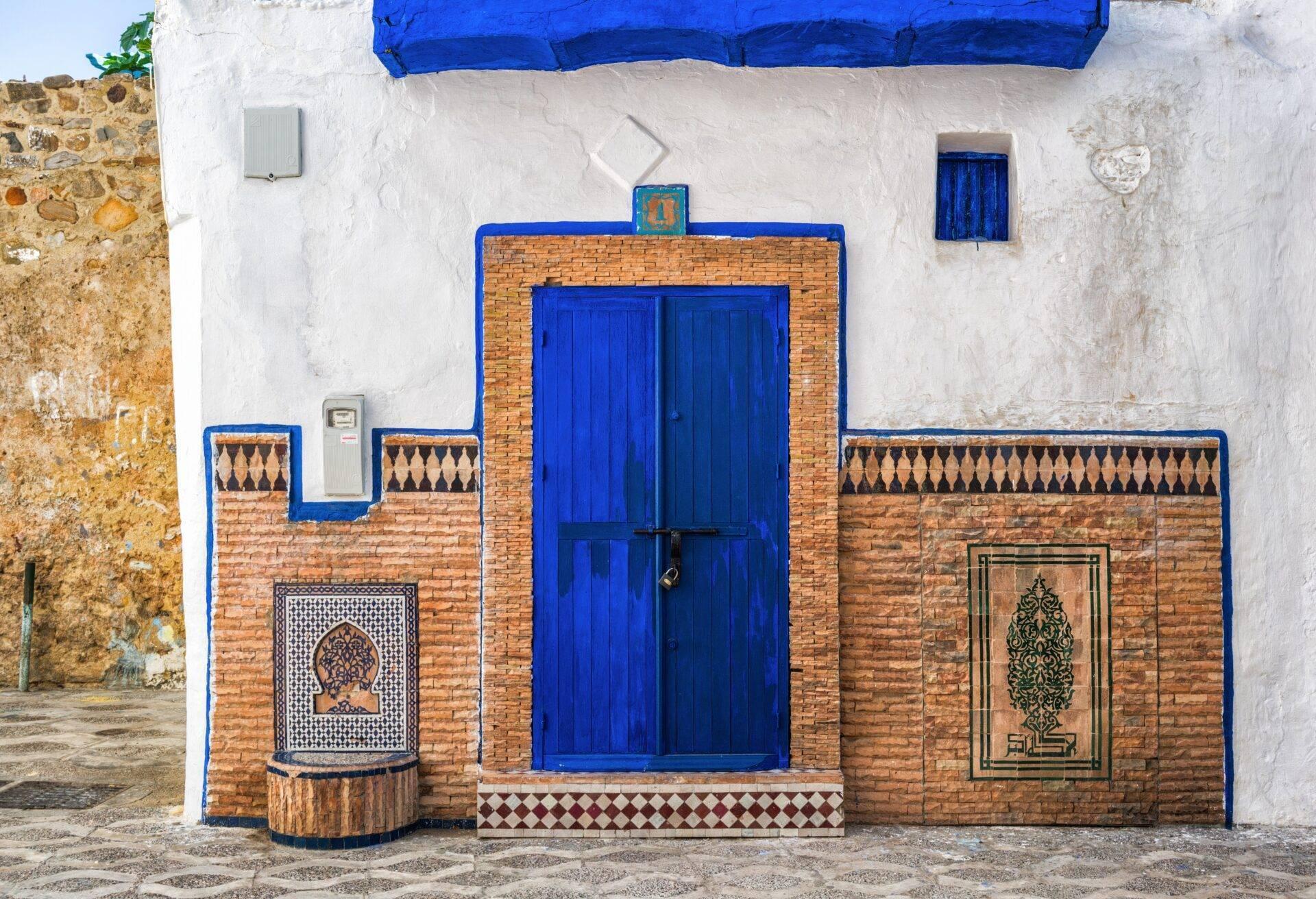Traditionelle marokkanische Hausfassade mit blauer Tür, Zellige-Details und charakteristischem Rot, Weiß und Blau