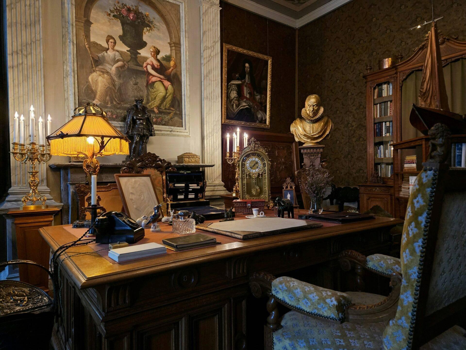 Historisch eingerichtetes Arbeitszimmer mit Holzschreibtisch, Büsten, alten Gemälden und goldenen Kerzenleuchtern