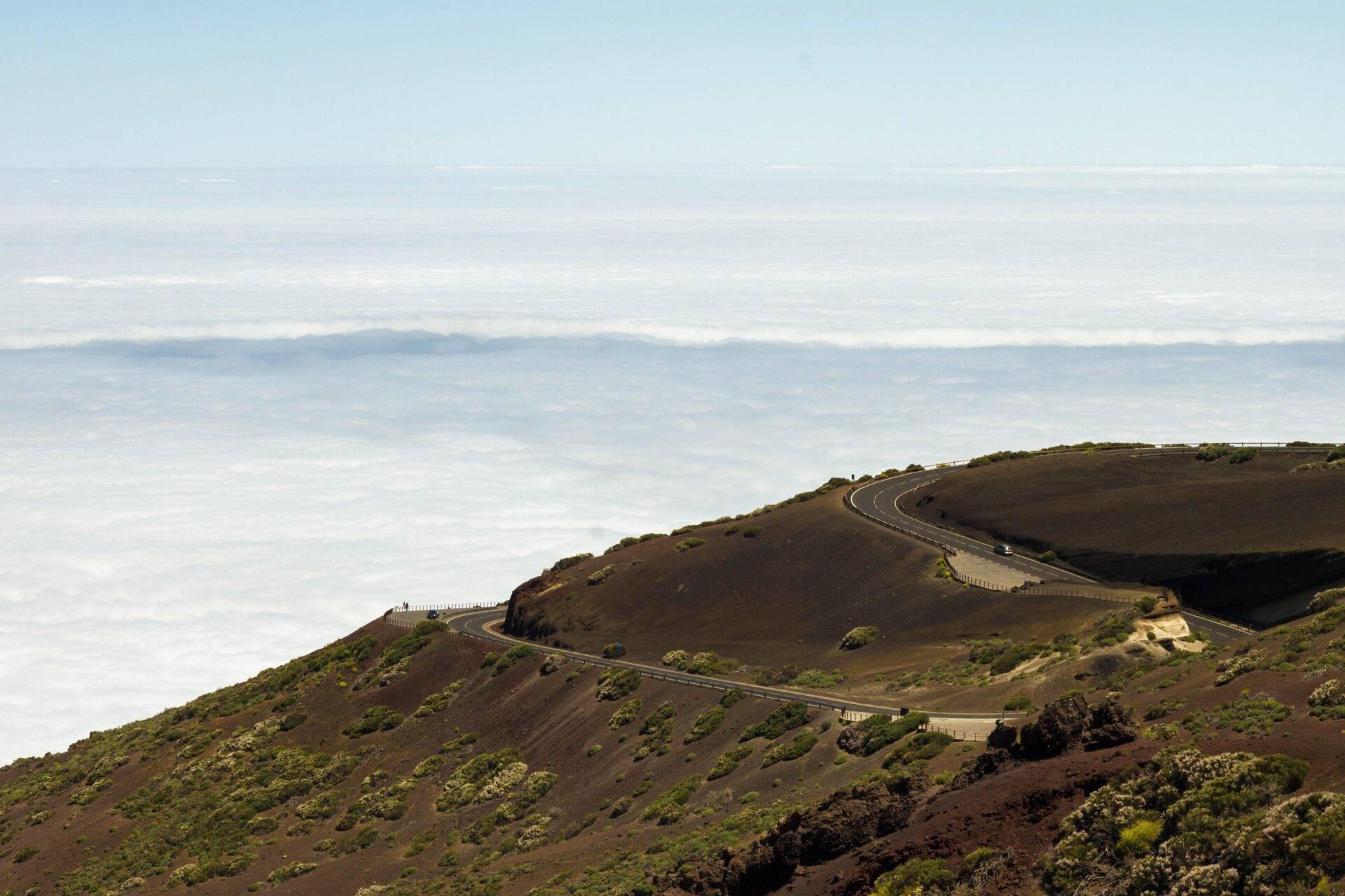 Strada tortuosa che attraversa un cratere vulcanico arido con vista sul mare e sulle nuvole sullo sfondo