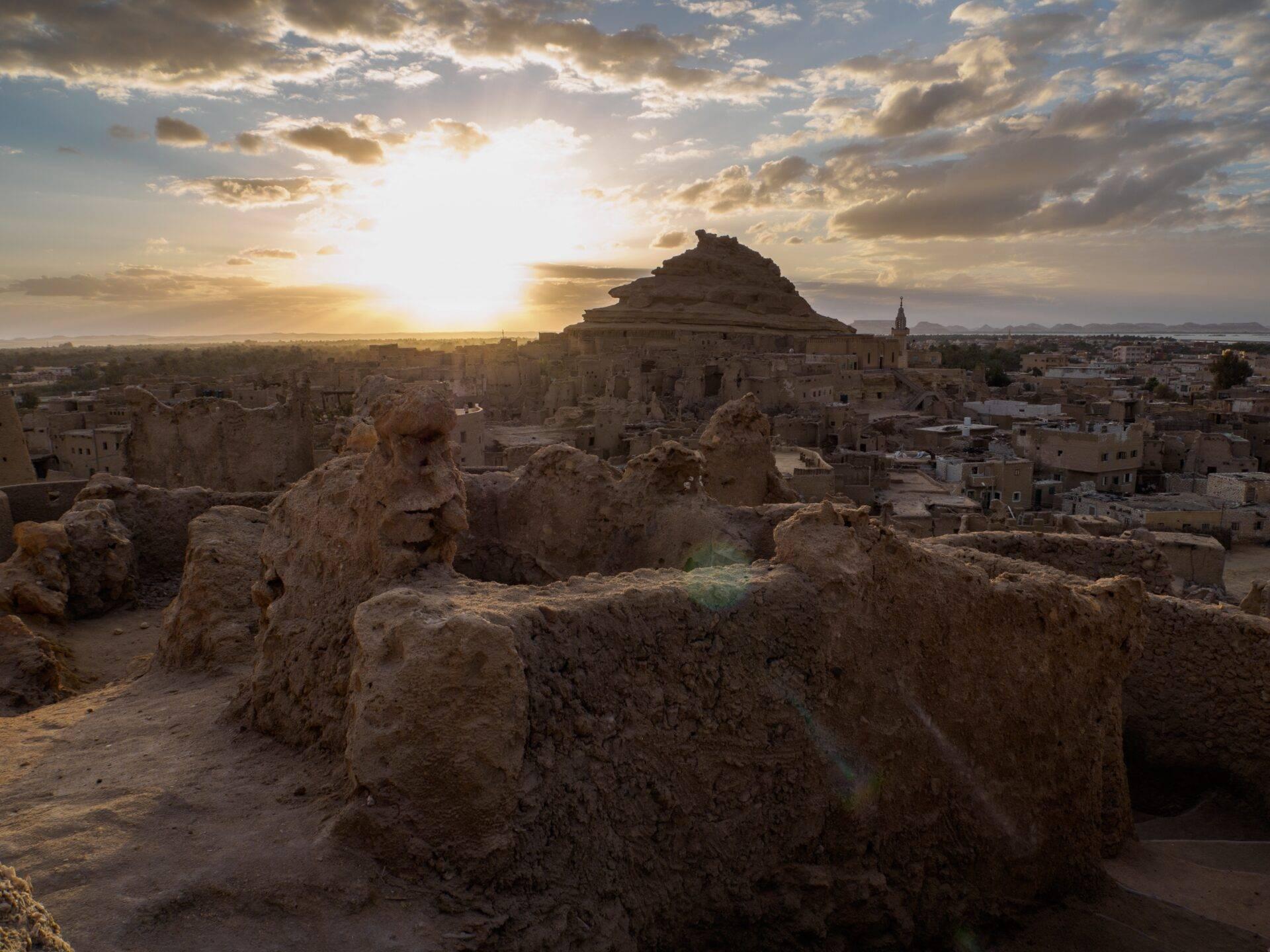 Vista panoramica di un’antica cittadella in pietra al tramonto che domina un villaggio desertico in Egitto