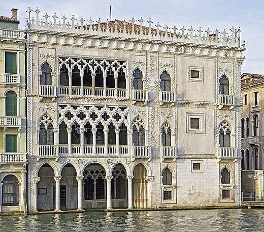 Facciata gotica veneziana in marmo bianco e rosa con arcate ogivali riflesse nell’acqua del canale