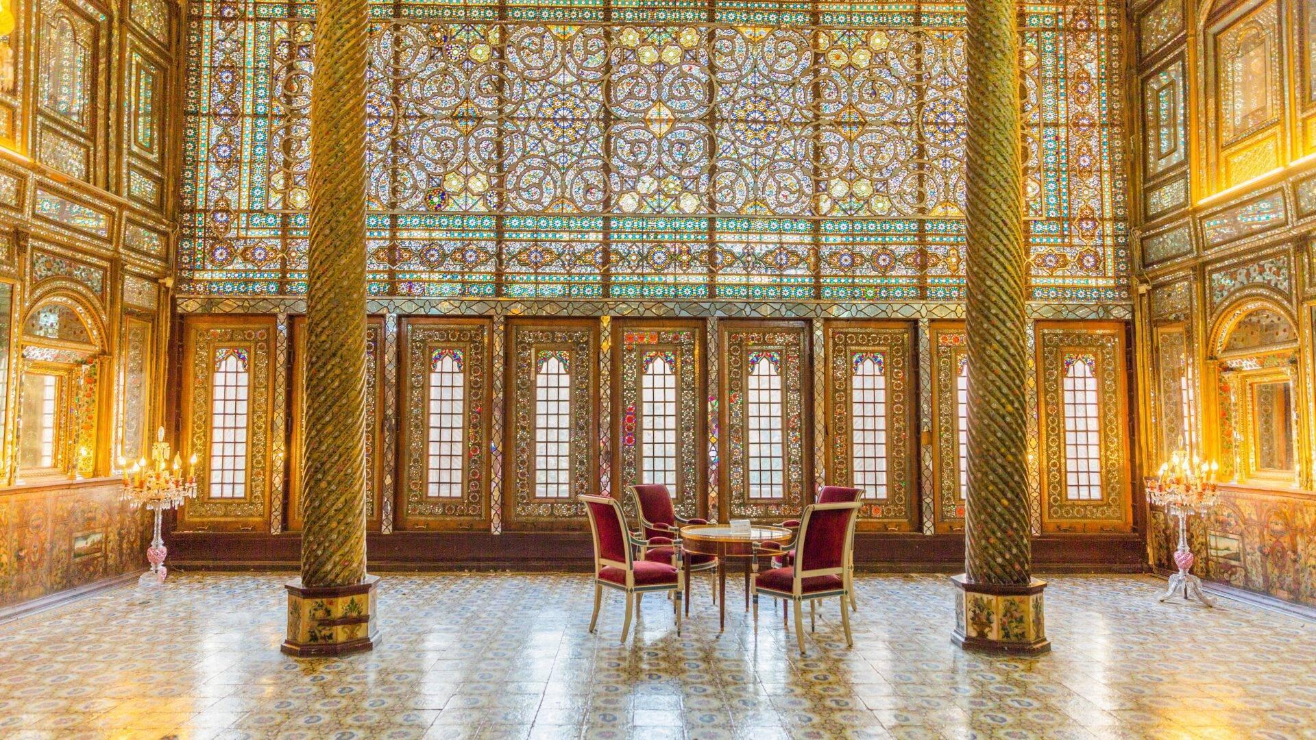 Mit Goldelementen und türkisfarbenen Mosaiken verzierter Saal mit goldenen Säulen und roten Stühlen