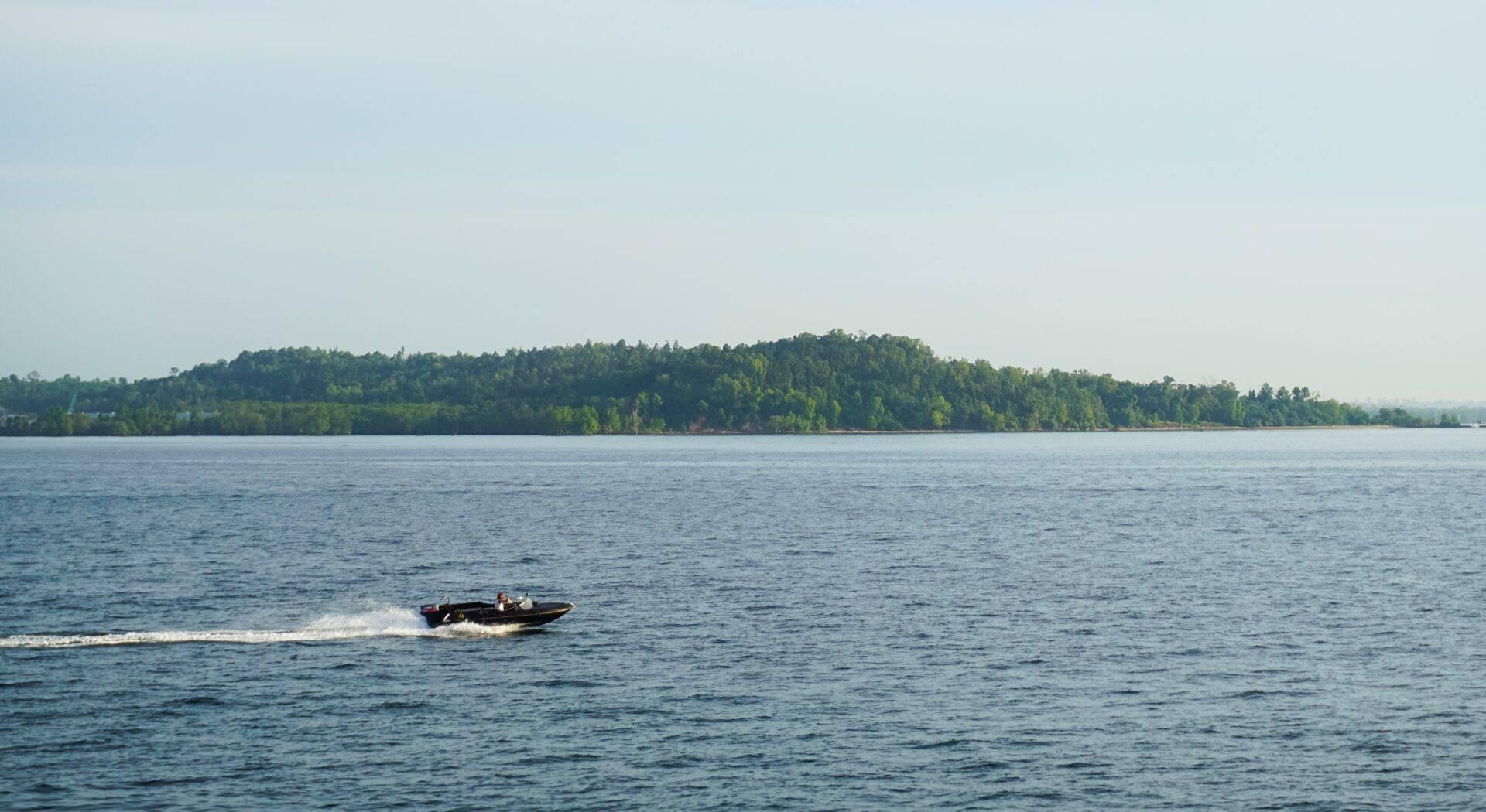 Un motoscafo naviga su un lago dalle acque calme bordato da una foresta fitta e verdeggiante