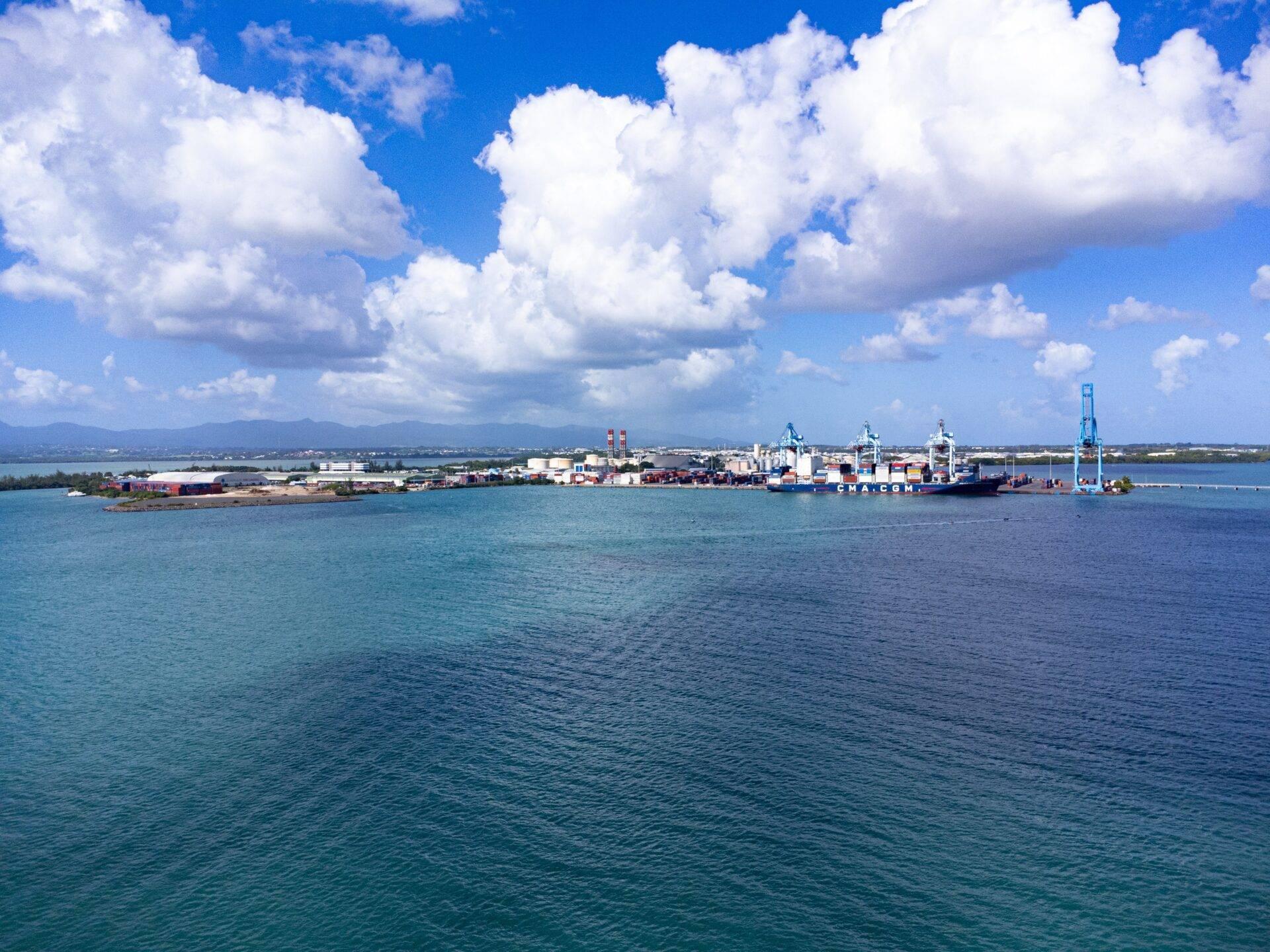 Panoramablick auf einen tropischen Seehafen mit Frachtschiff, Hafenanlagen und Bergen im Hintergrund
