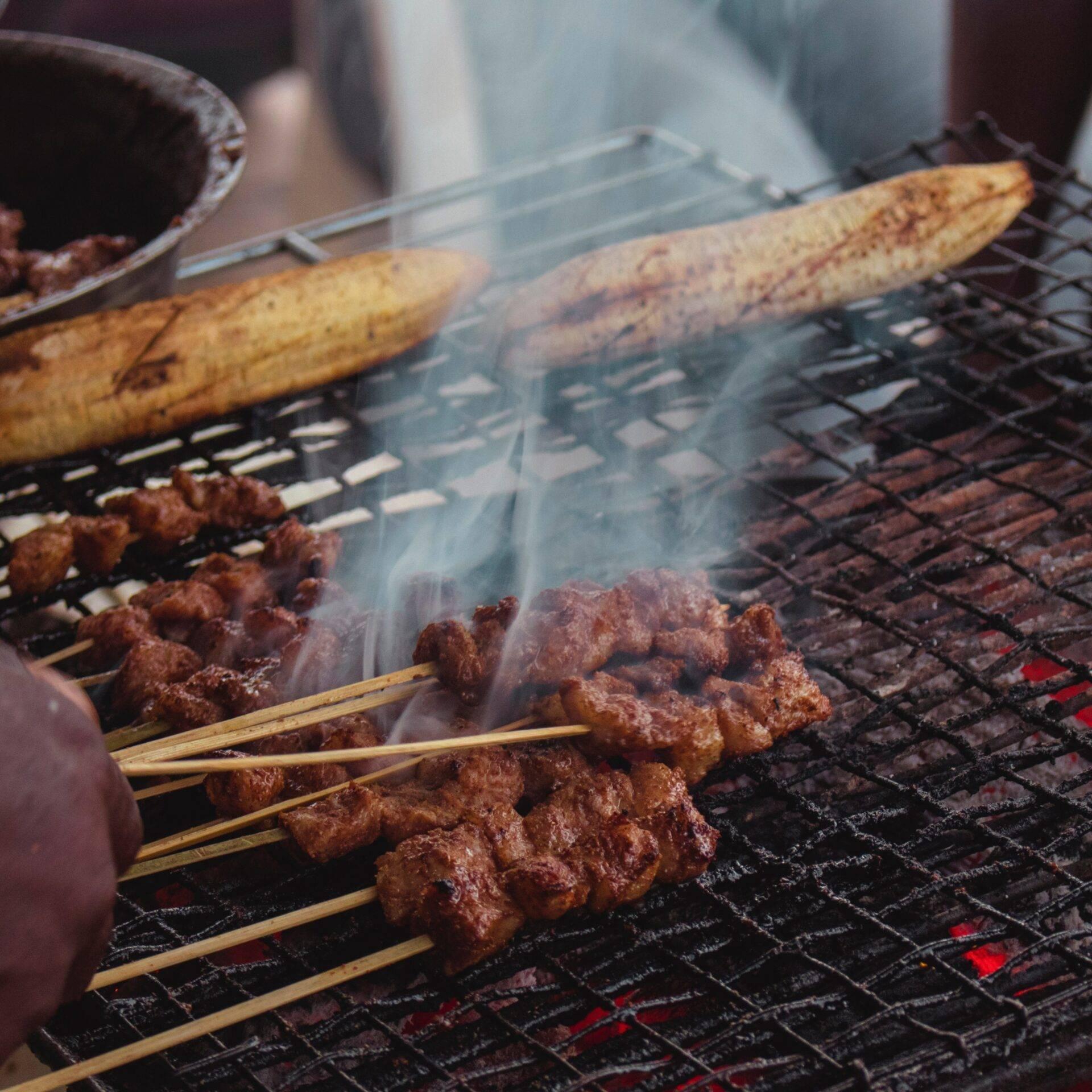 Brochetas de carne a la brasa sobre una parrilla humeante con plátanos macho, cocina tradicional camerunesa
