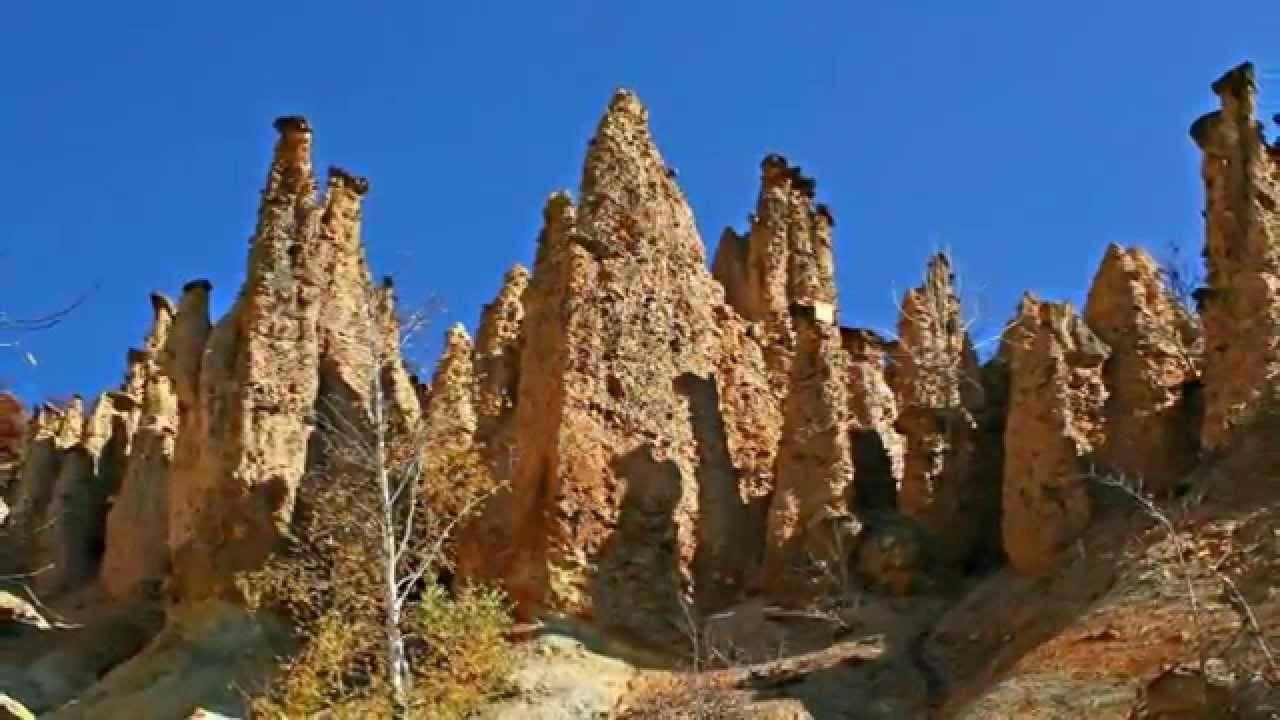 Spektakuläre Felsformation mit ockerfarbenen Sandsteintürmen und spärlicher Vegetation unter klarem blauem Himmel