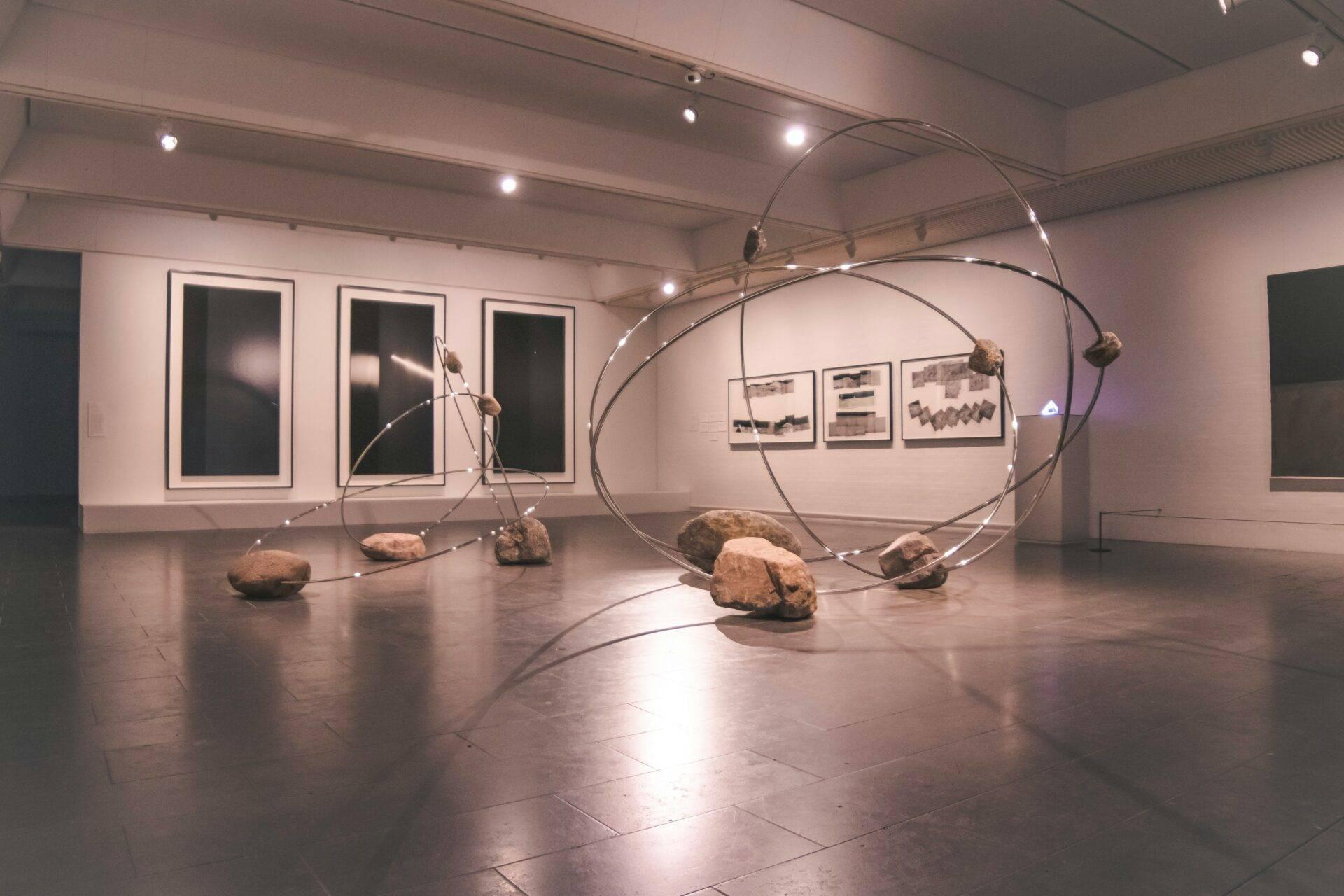 Installazione artistica contemporanea con strutture metalliche curve e rocce in una galleria d’arte minimalista