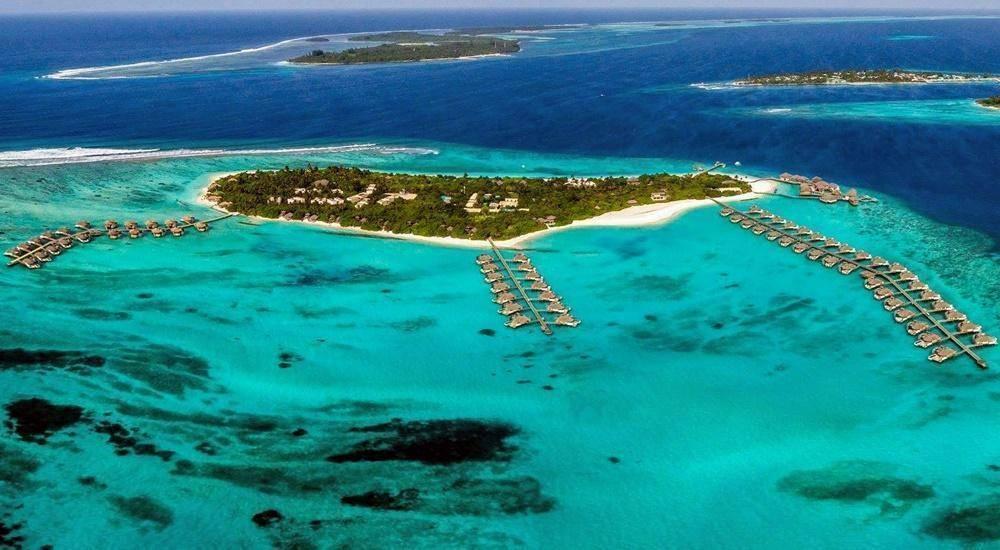 Vista aerea di un’isola tropicale circondata da bungalow sull’acqua in una laguna turchese dalle acque cristalline