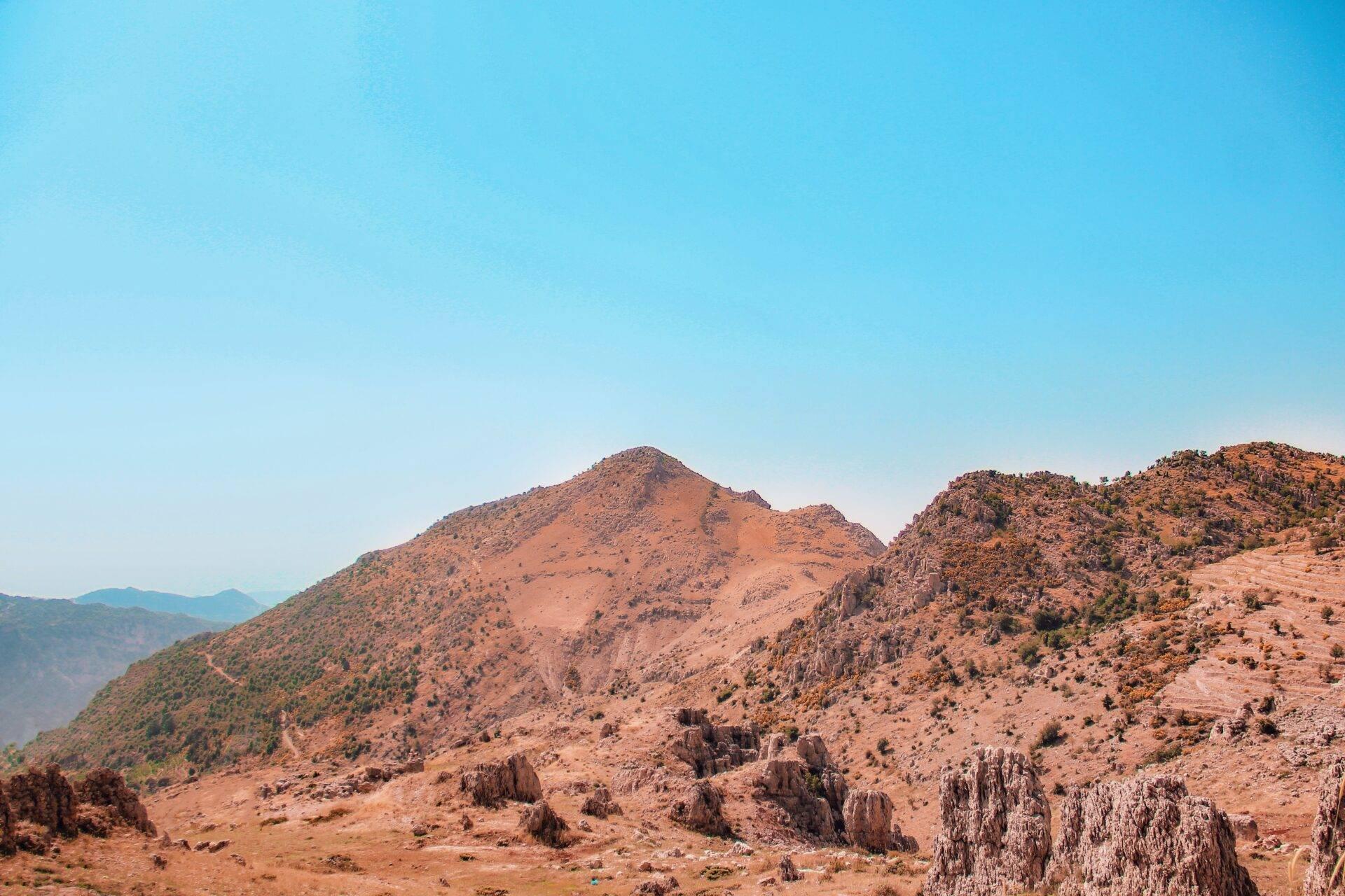 Paisaje montañoso árido con formaciones rocosas, vegetación dispersa y cadenas de montañas al fondo bajo un cielo despejado