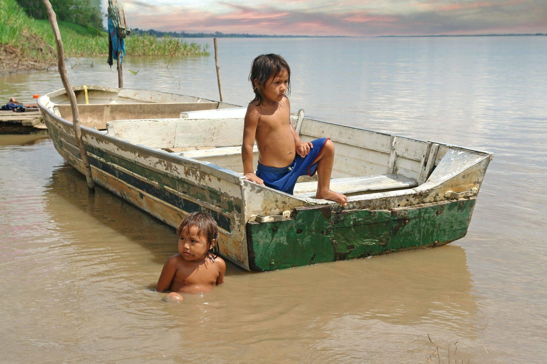 Dos niños juegan en el agua junto a viejas barcas de pesca de madera cerca de una costa pantanosa