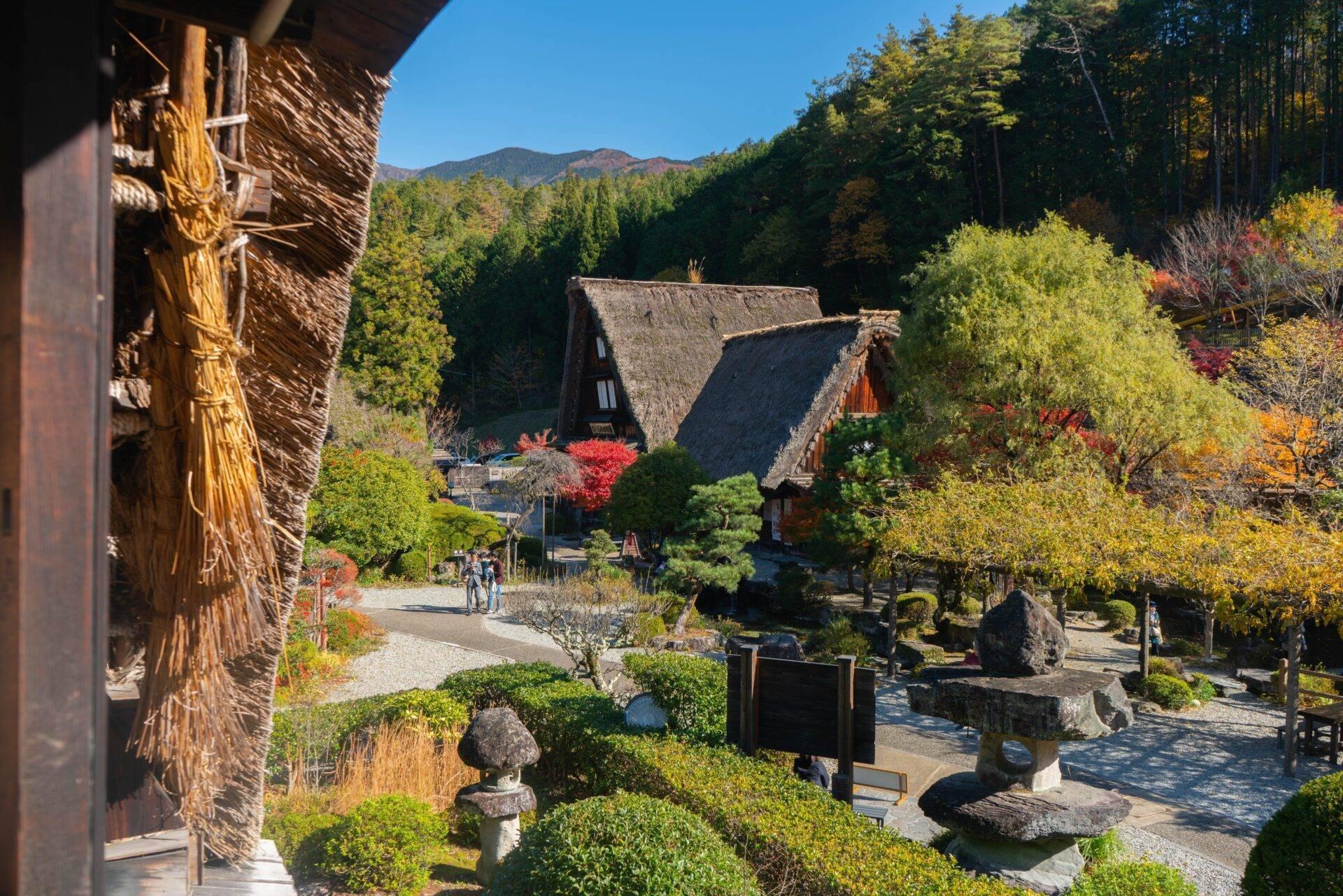 Traditionelles japanisches Dorf mit Strohdachhäusern, angelegten Gärten und bewaldeten Bergen im Hintergrund