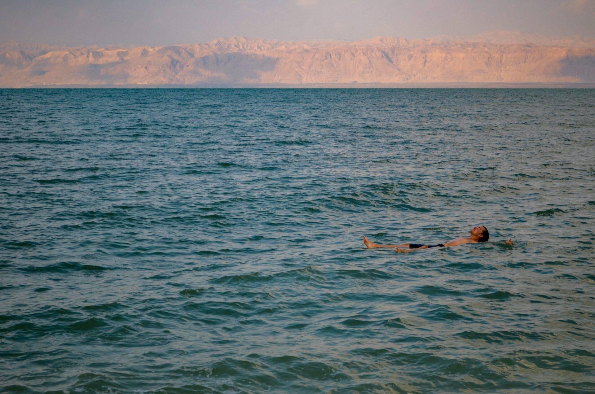 Un hombre flota sin esfuerzo en aguas turquesas frente a majestuosos acantilados ocres desérticos
