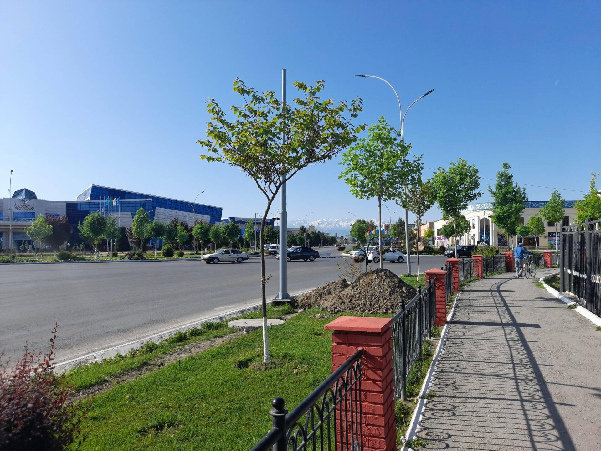 Moderne Stadtstraße in Zentralasien mit modernen Gebäuden, breiter Fahrbahn und schneebedeckten Bergen im Hintergrund