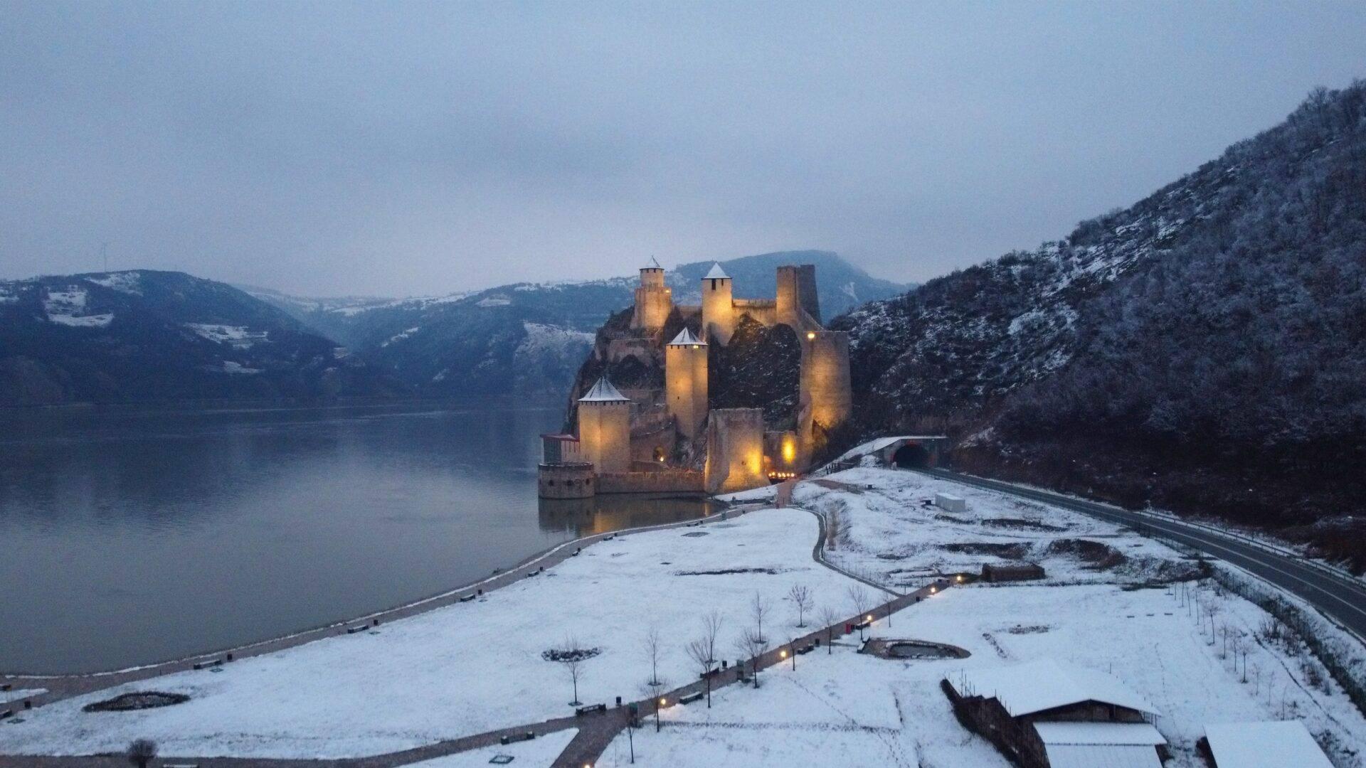 Eine beleuchtete mittelalterliche Burg in der Abenddämmerung auf einer felsigen Halbinsel über einem zugefrorenen See im Winter