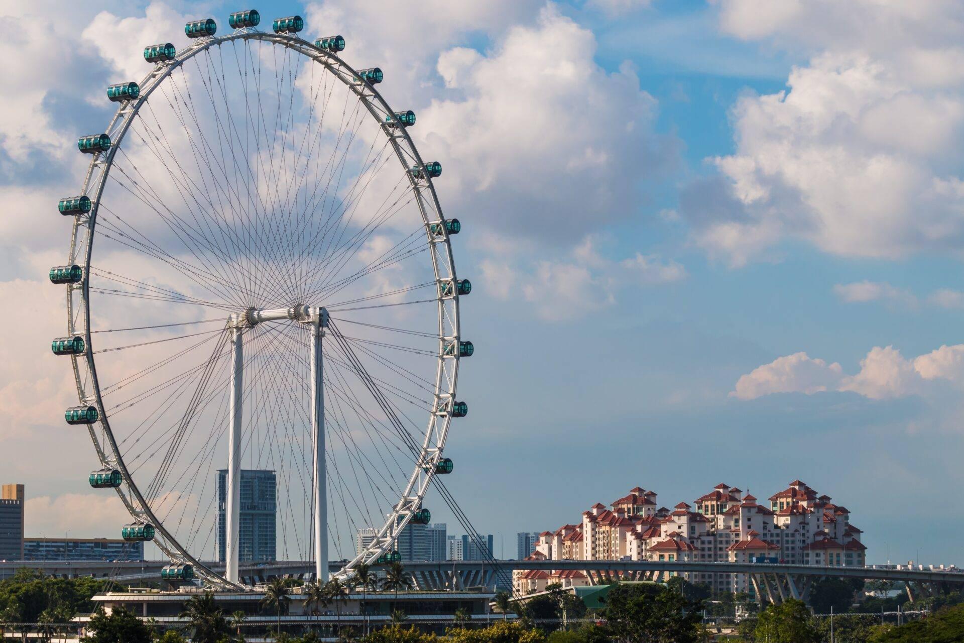 Ein weißes Riesenrad mit grünen Gondeln überragt Wolkenkratzer und Wohngebäude unter einem leicht bewölkten blauen Himmel
