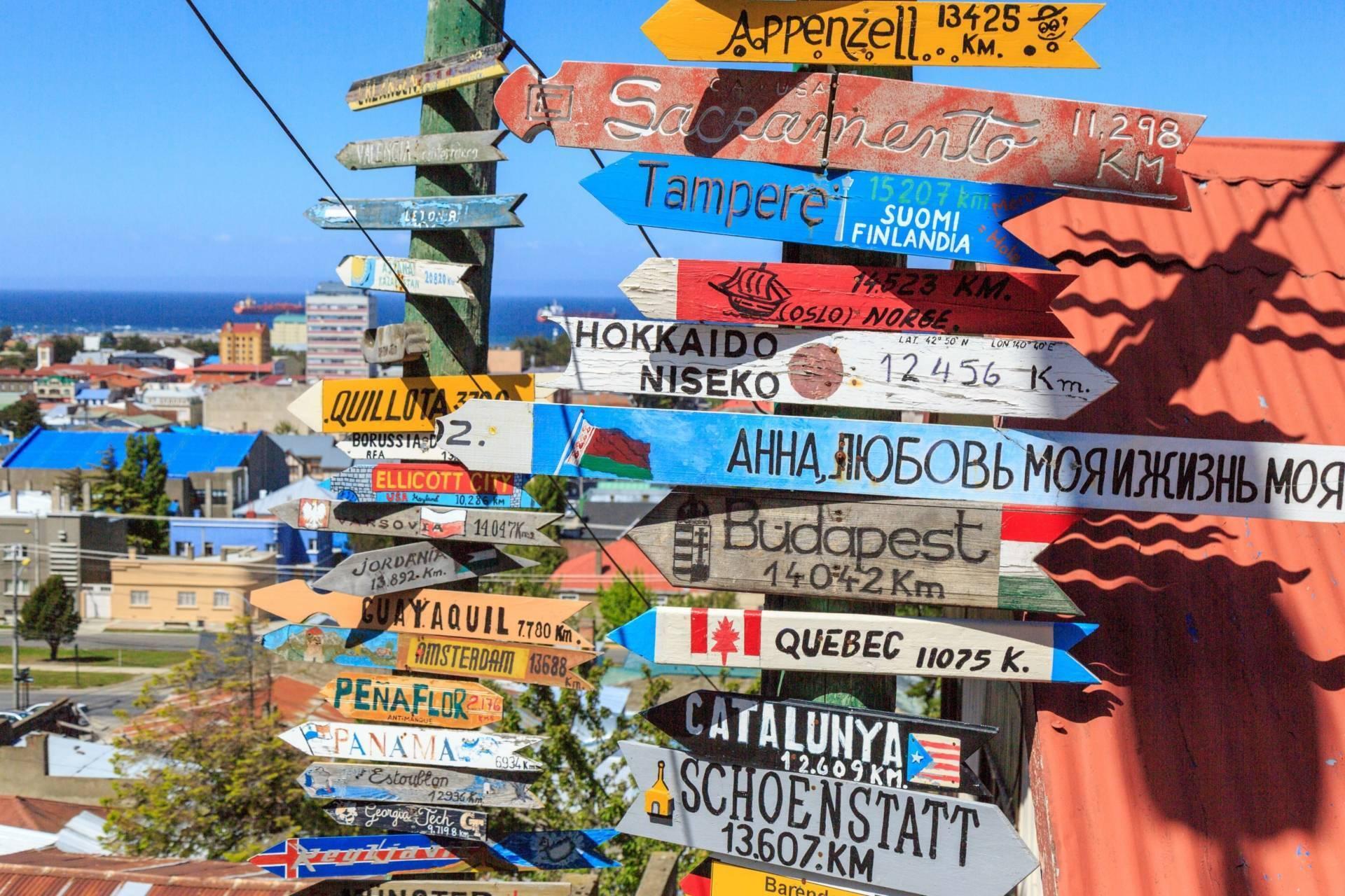Un poste indicador de colores con flechas que señalan destinos de todo el mundo, con vistas a la costa y edificios al fondo