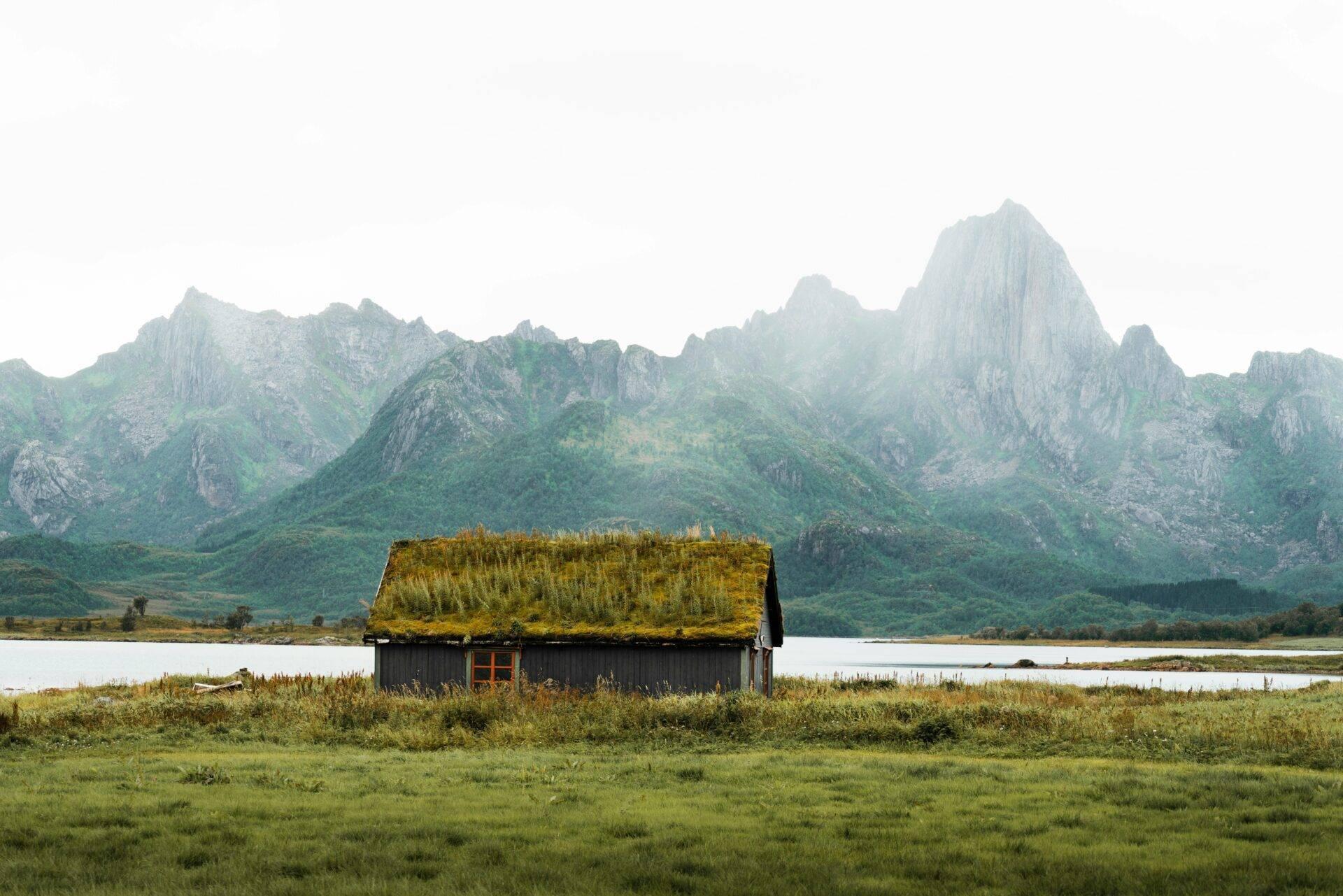 Eine Hütte mit Moosrasen auf dem Dach vor einem See und grün-felsiger Berglandschaft in Norwegen