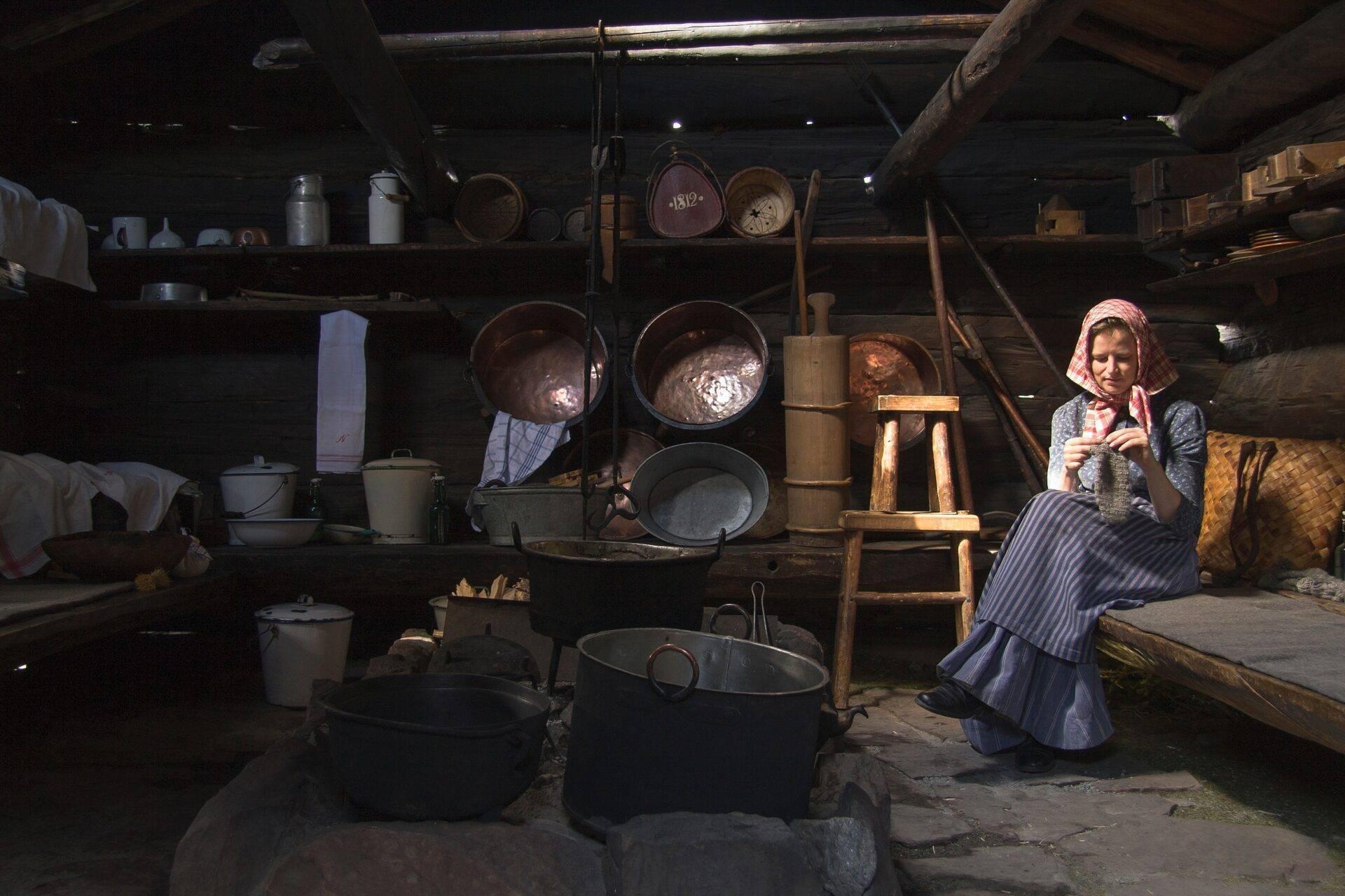Eine Frau in Tracht arbeitet in einer historischen Küche mit Gerätschaften und Möbeln vergangener Epochen