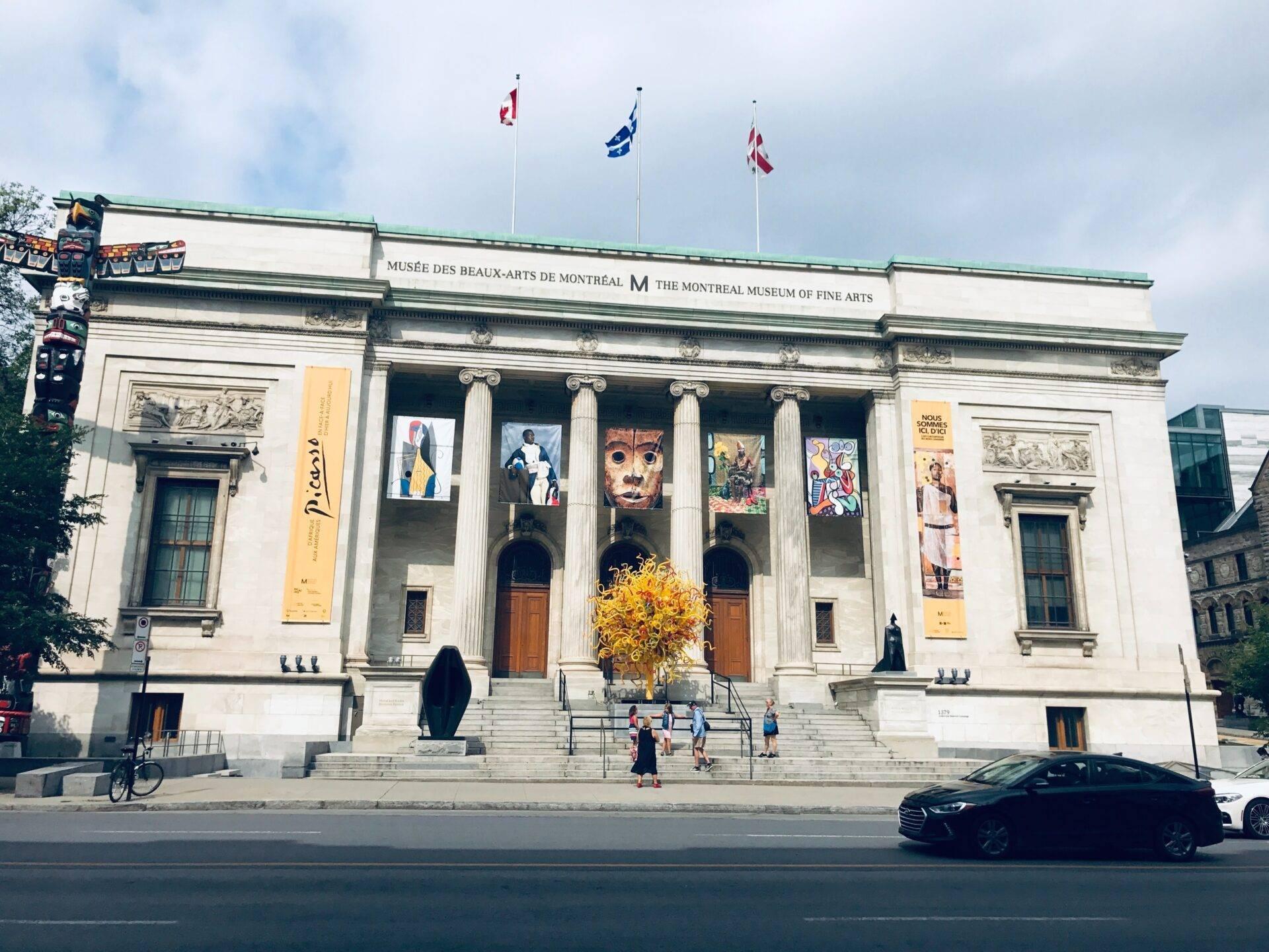 Klassische Fassade eines Kunstmuseums mit weißen Säulen, Fahnen und gelben Ausstellungsbannern