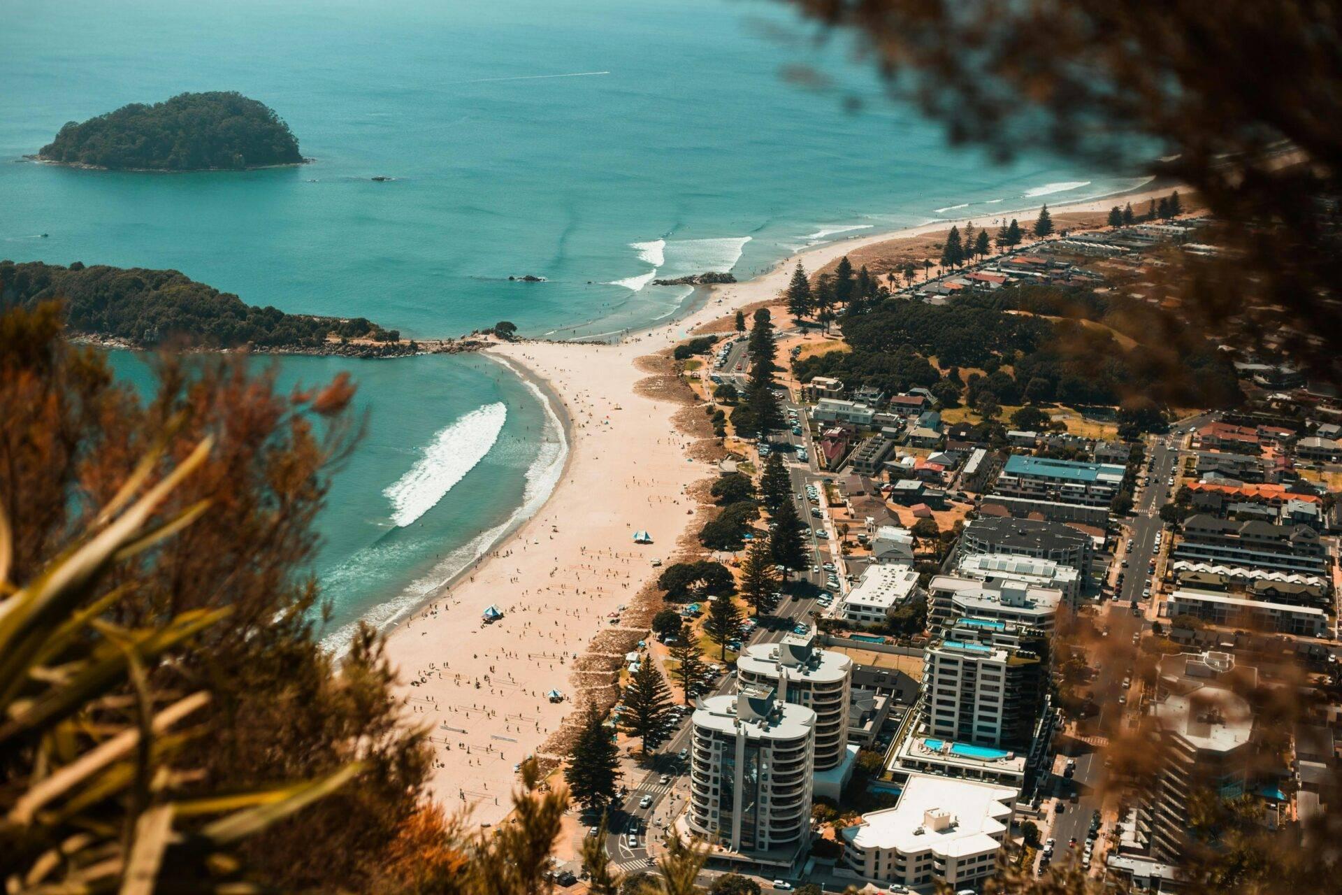 Vista aerea di una spiaggia urbana con grattacieli, isolotto boscoso e acque turchesi cristalline