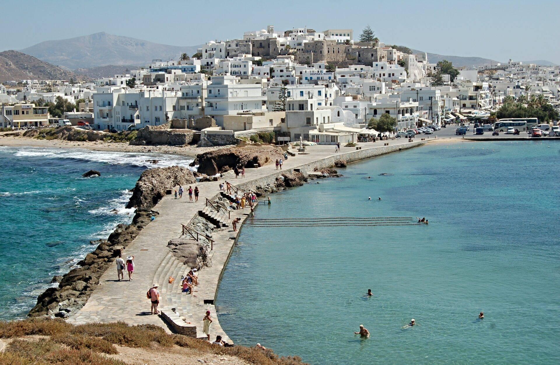 Ein weißes mediterranes Küstendorf auf einem Hügel mit türkisfarbenem Strand und belebter Felsküste