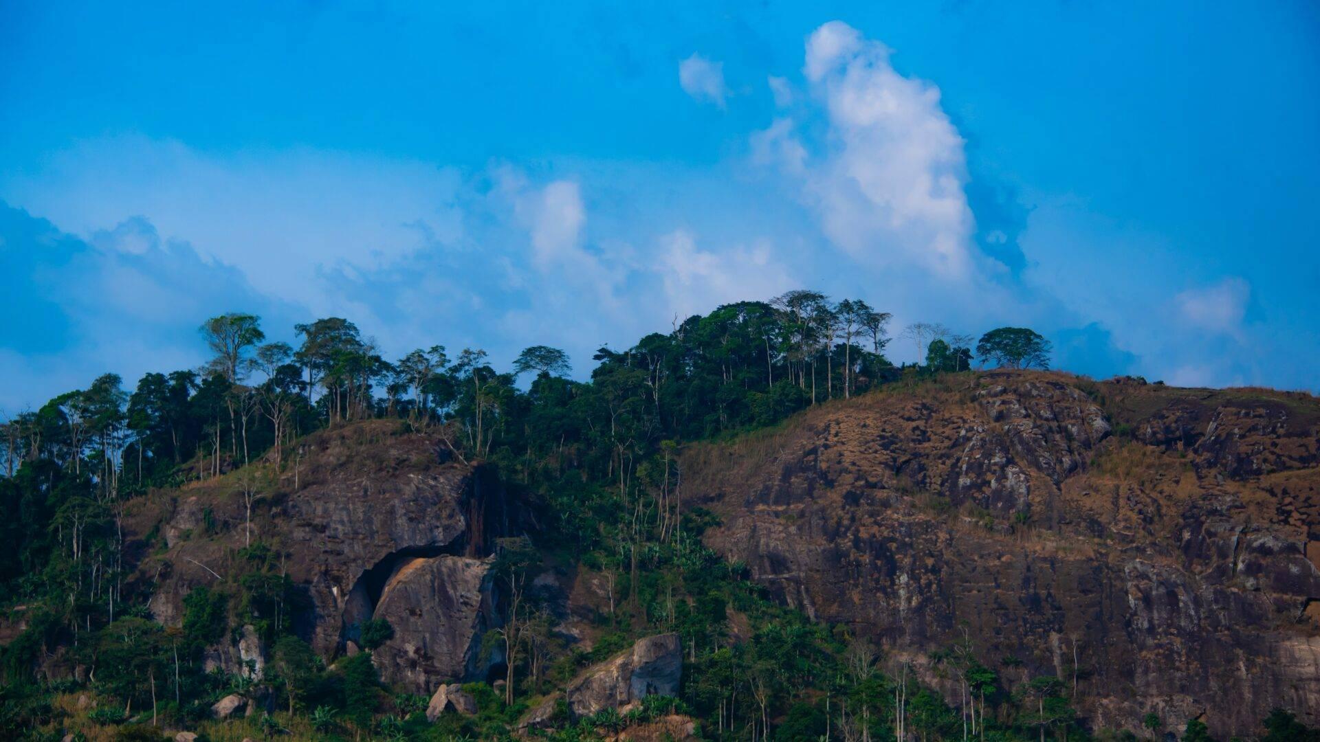 Paisaje montañoso con afloramientos rocosos, densa vegetación tropical y cielo azul nublado