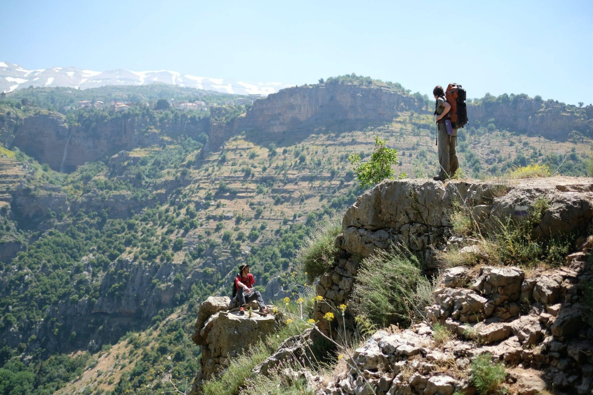 Dos senderistas sobre unas rocas con vistas a un cañón montañoso boscoso de acantilados espectaculares