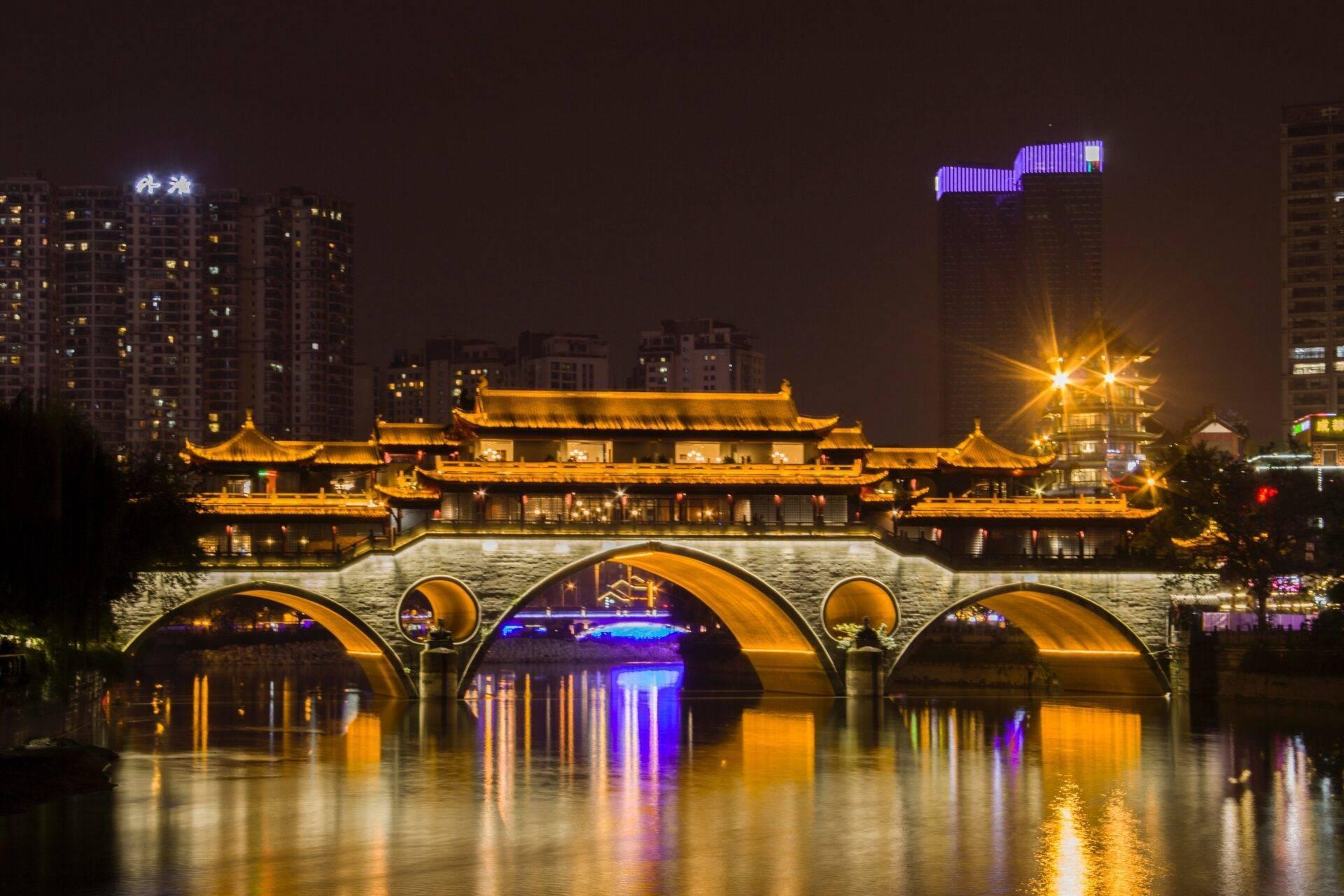 Un tempio tradizionale asiatico illuminato di notte con un ponte in pietra ad arco che attraversa un fiume