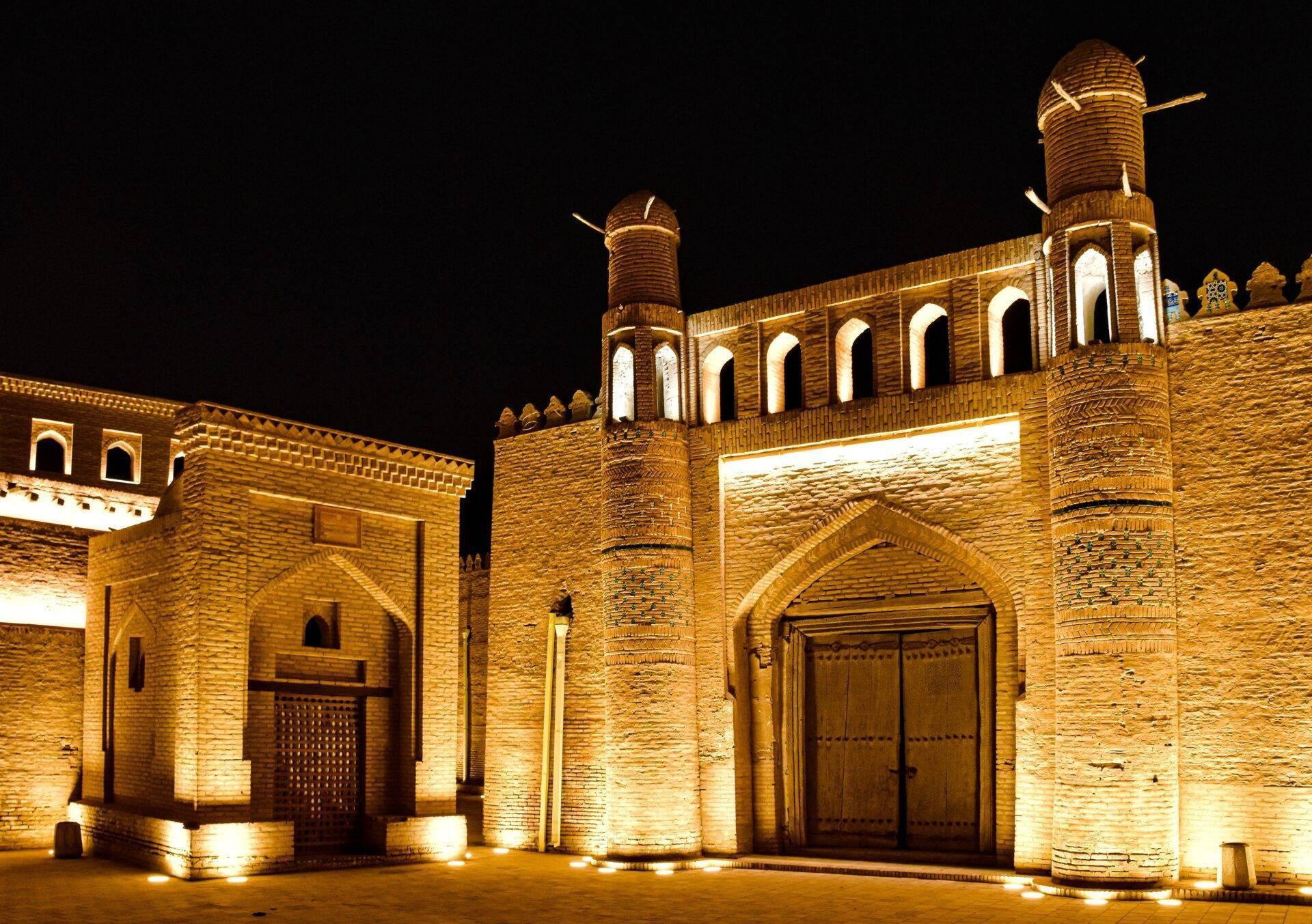 Historische Backsteinmoschee bei Nacht, beleuchtet, mit Minaretten und charakteristischer Arkadenarchitektur Zentralasiens