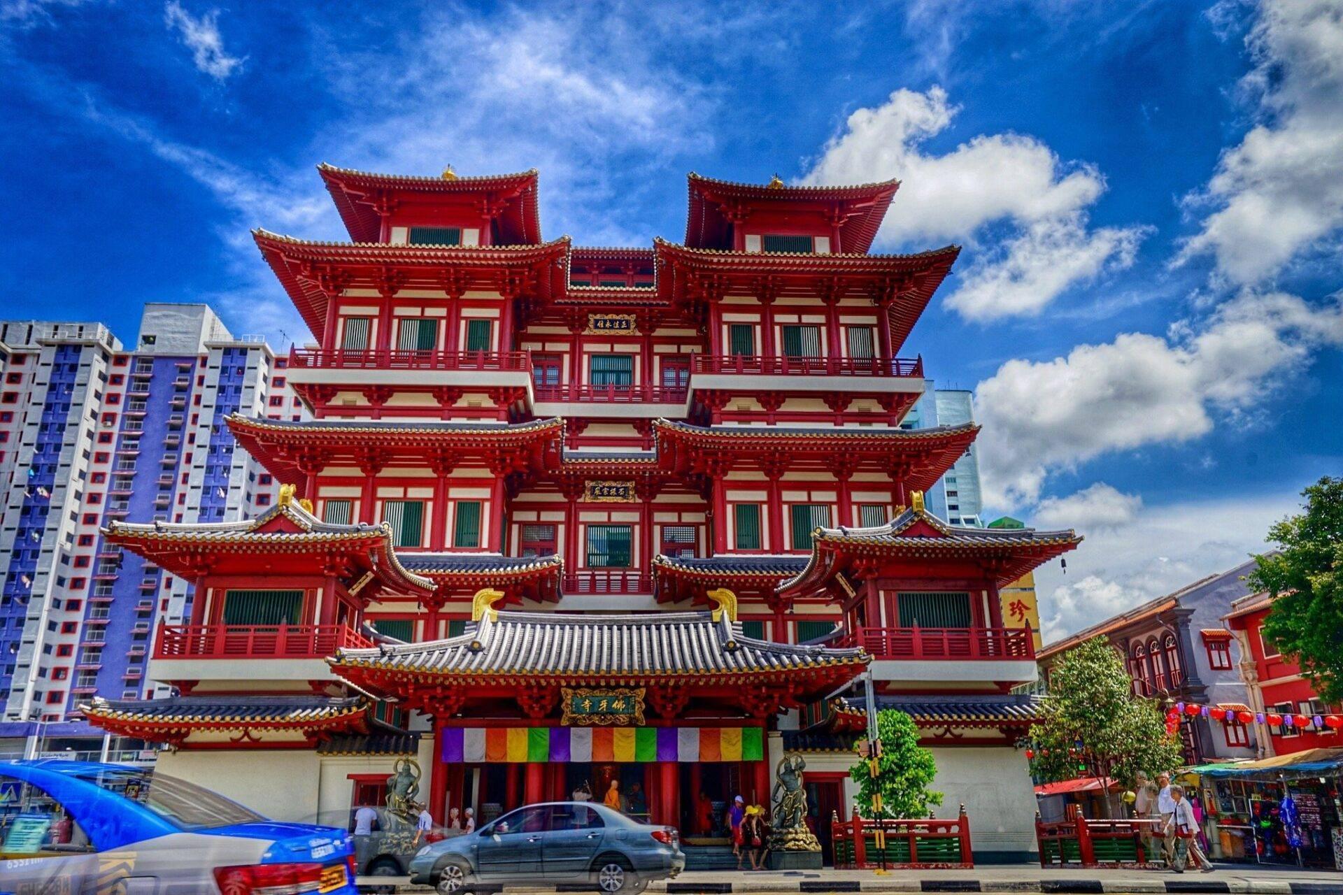 Ein roter buddhistischer Tempel im Tang-Stil mit charakteristischen spitzen Dächern, umgeben von modernen Gebäuden unter blauem Himmel