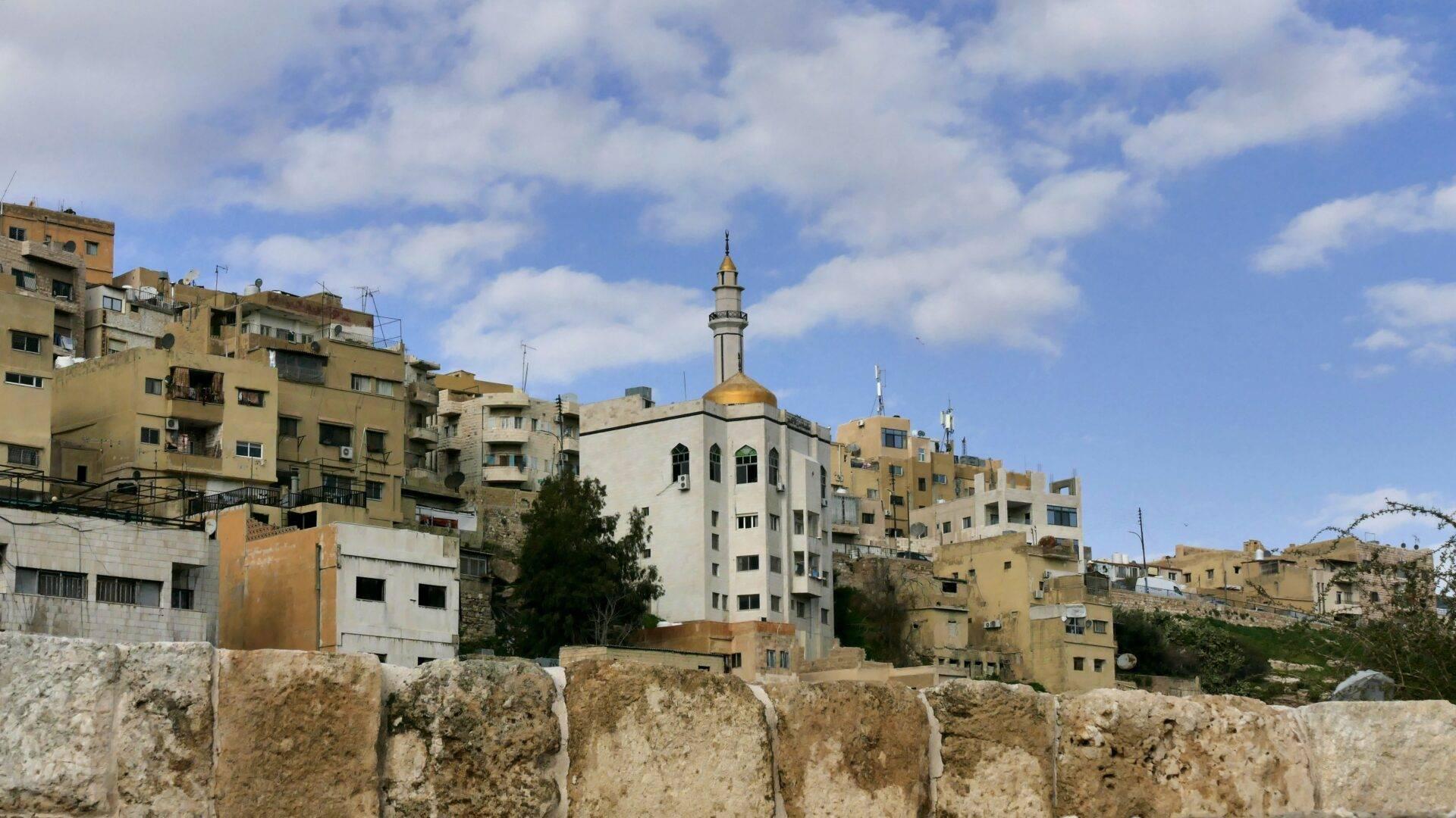 Vista de una ciudad de Oriente Próximo con mezquita de cúpula dorada rodeada de edificios de piedra beige y muro de fortificación