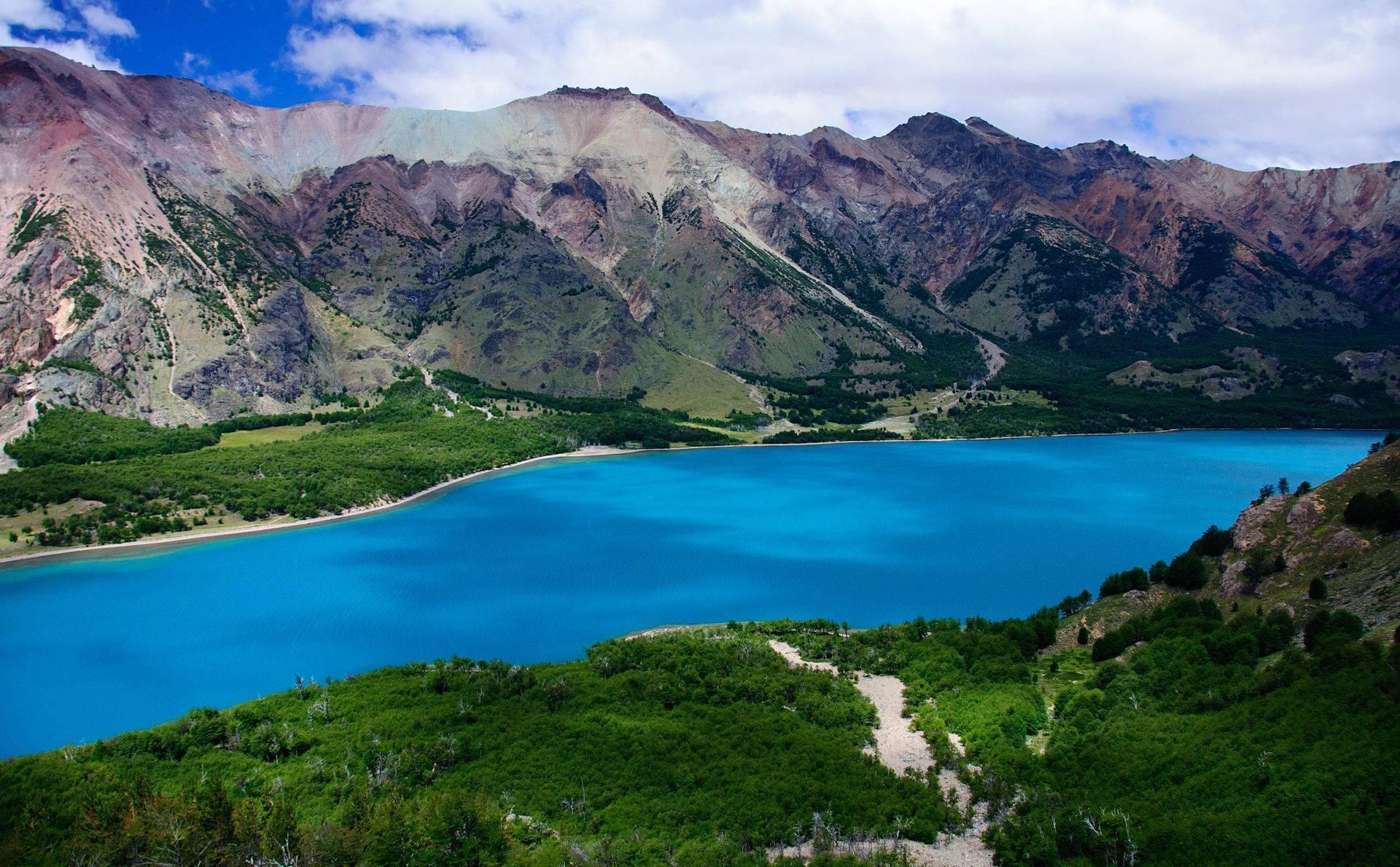Un lago alpino de un azul turquesa intenso enmarcado por montañas de colores y exuberante vegetación verde
