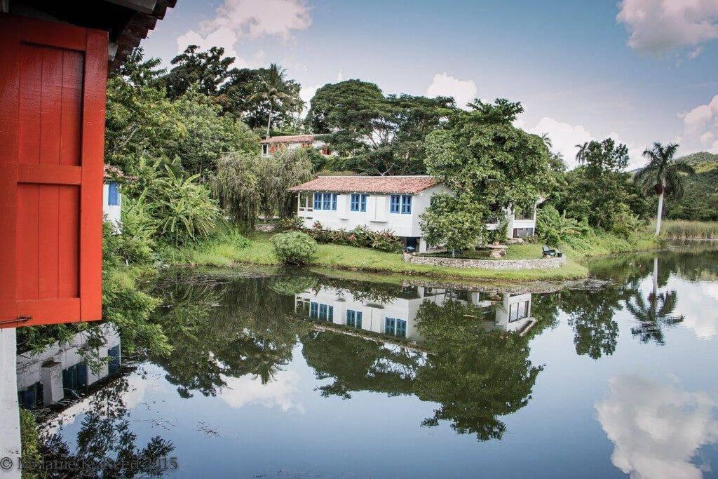 Case coloniali bianche e blu con porta rossa che si riflettono in un canale tropicale circondato da vegetazione lussureggiante
