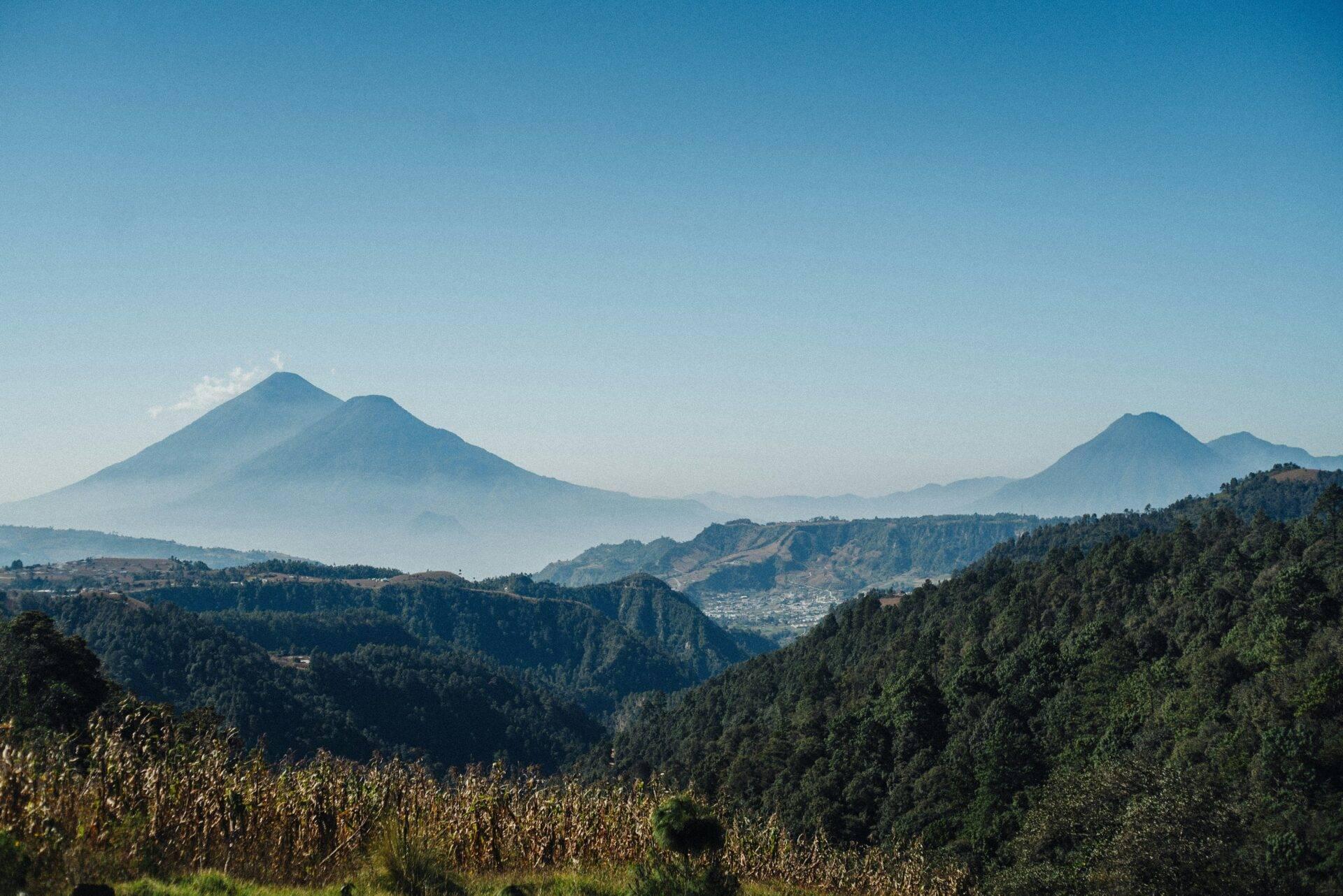 Gebirgslandschaft Guatemalas mit zwei schneebedeckten Vulkanen am Horizont, Kiefernwäldern und landwirtschaftlichen Feldern