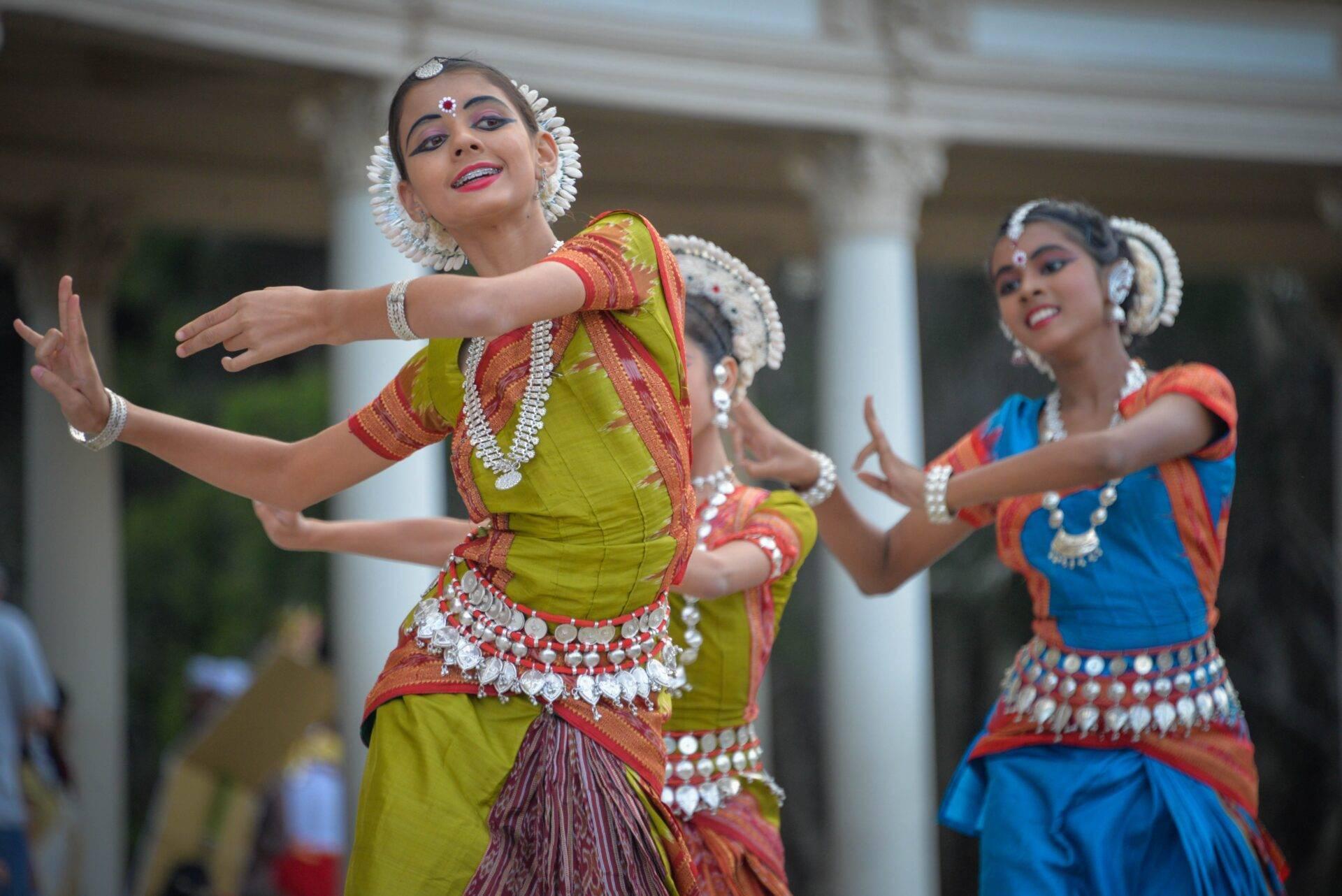 Tänzerinnen in bunten traditionellen Kostümen bei einer klassischen indischen Tanzvorführung vor Kolonialarchitektur