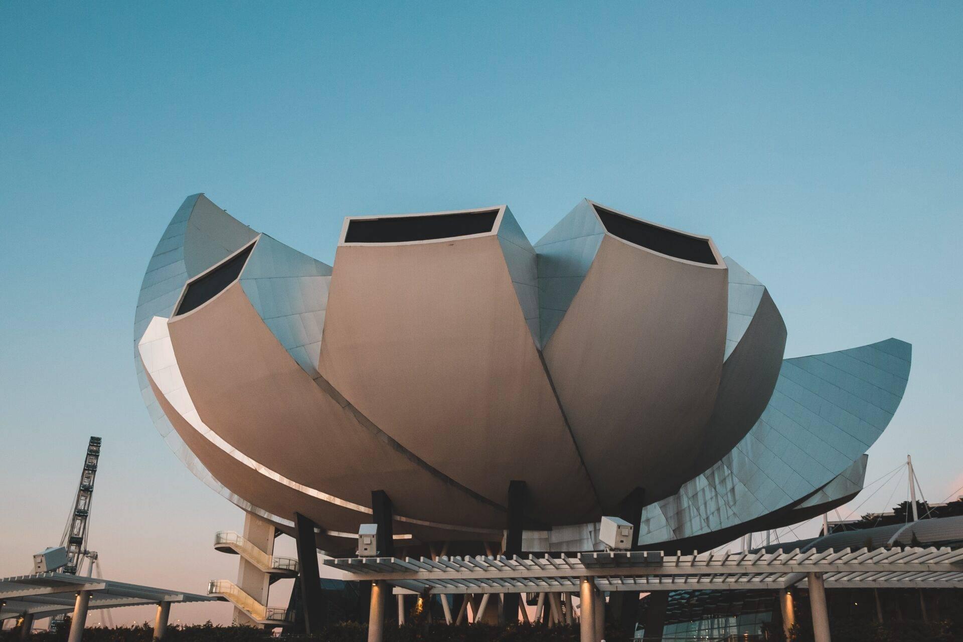 Ein modernes Gebäude in Lotusform mit metallischen Blütenblättern und Glasfassade unter klarem blauem Himmel