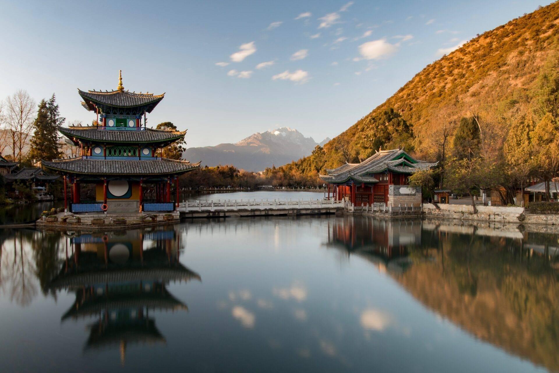 Un tempio asiatico a tre piani si riflette in un lago tranquillo, incorniciato da montagne boscose e vette innevate