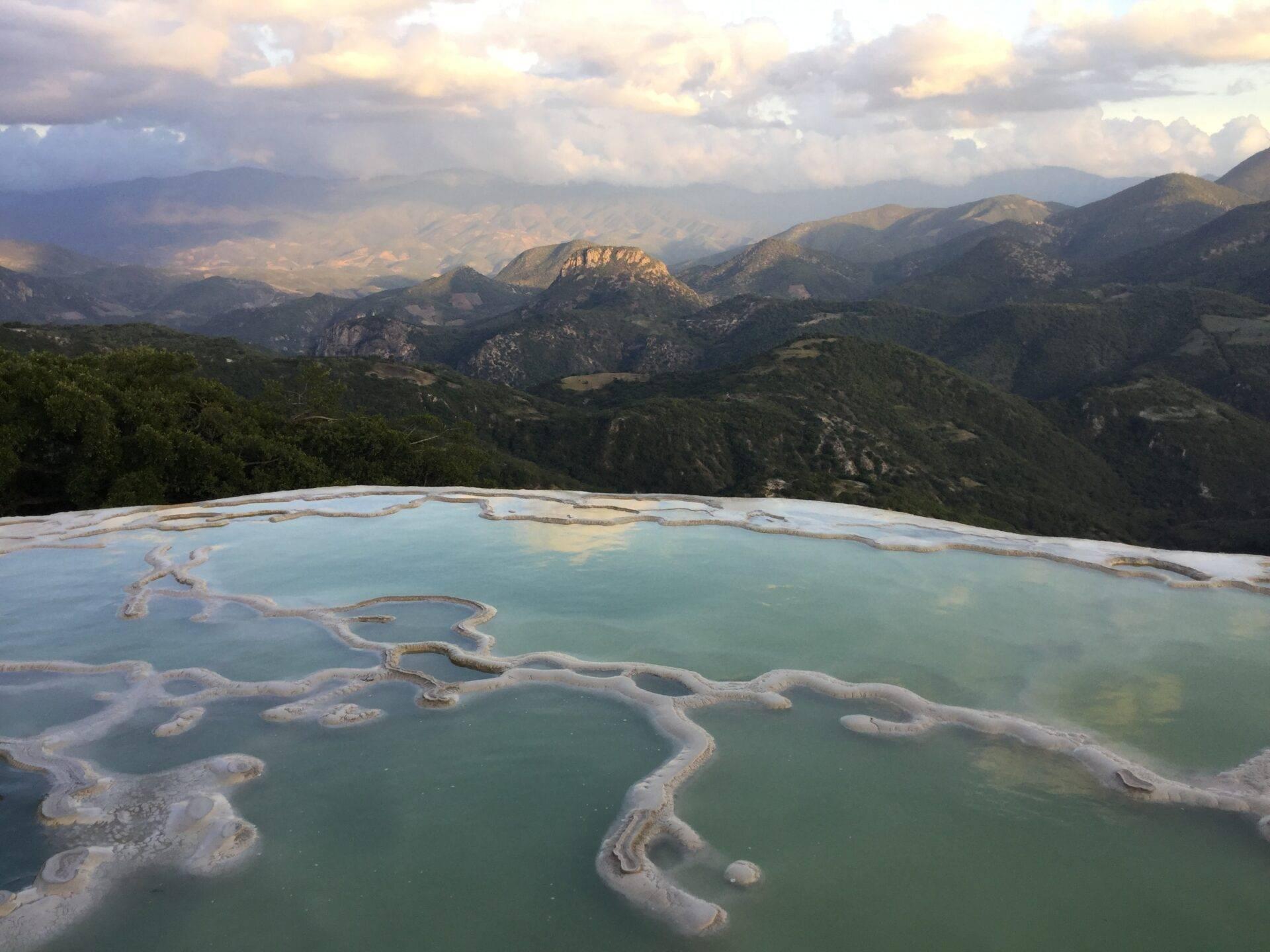 Türkisfarbene Thermalterrassen mit weißen Mineralablagerungen mit Blick auf ein grünes Bergtal