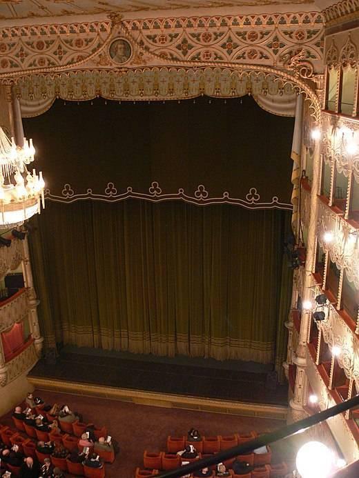 Interno ornamentato di un teatro storico con tendone verde scuro e balconi illuminati