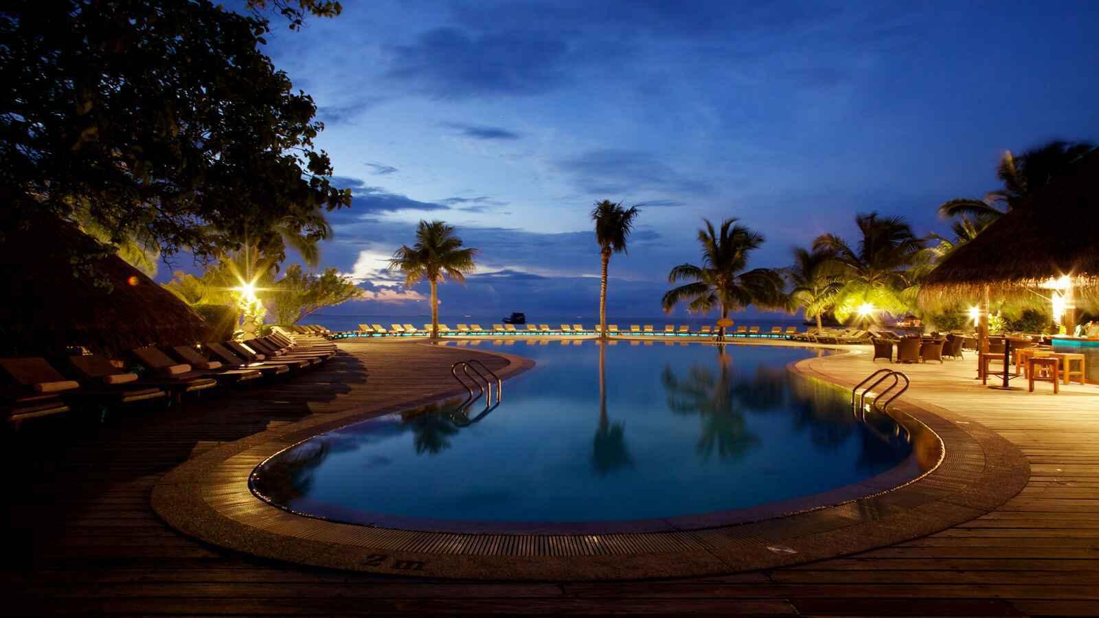 Una lussuosa piscina infinita illuminata al crepuscolo con palme e sdraio di fronte all’oceano