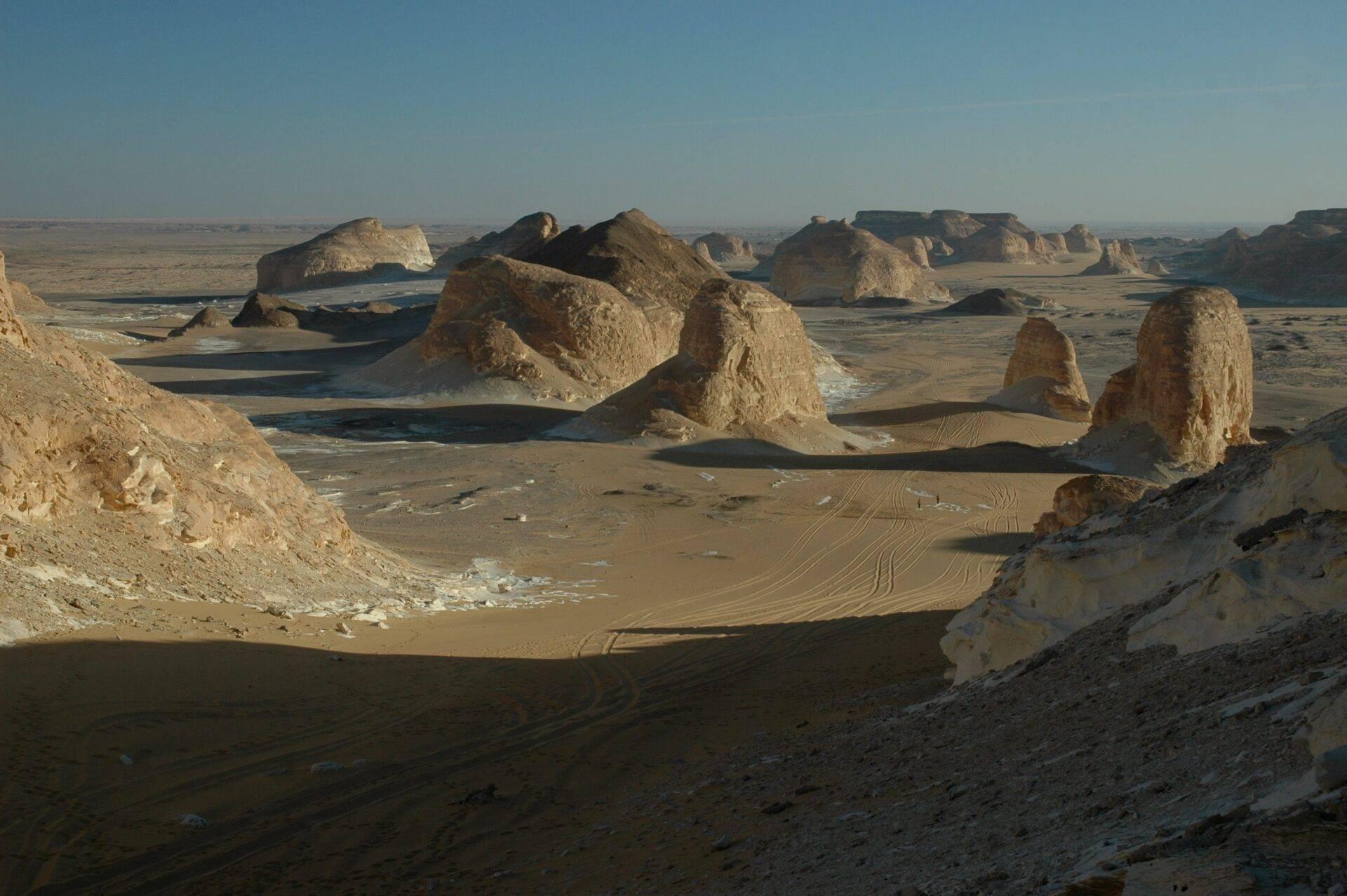 Spettacolari formazioni rocciose calcaree in un deserto arido con tracce di veicoli sul suolo sabbioso